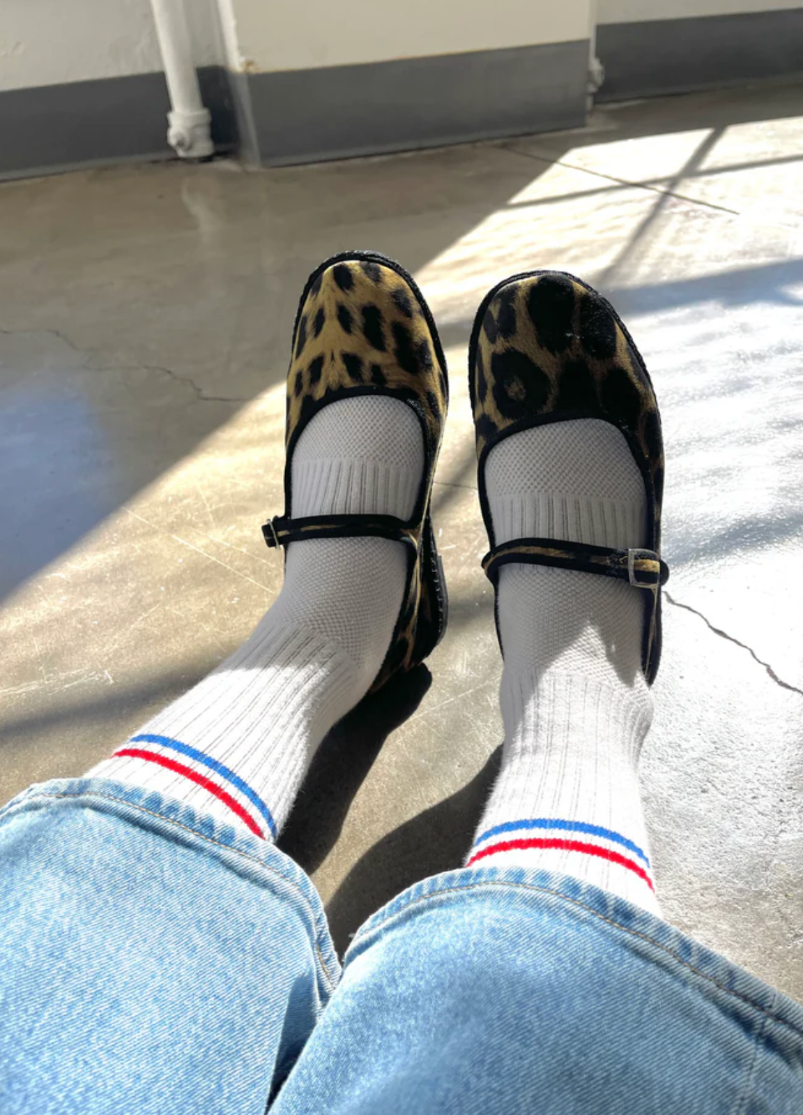 Leopard print shoes worn with white socks featuring red, blue, and yellow stripes on a concrete floor.