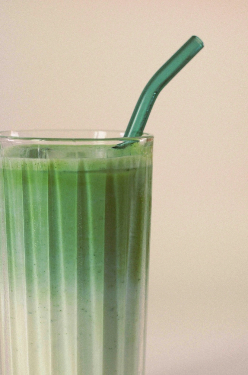 a creamy matcha beverage with a green glass straw in a glass cup