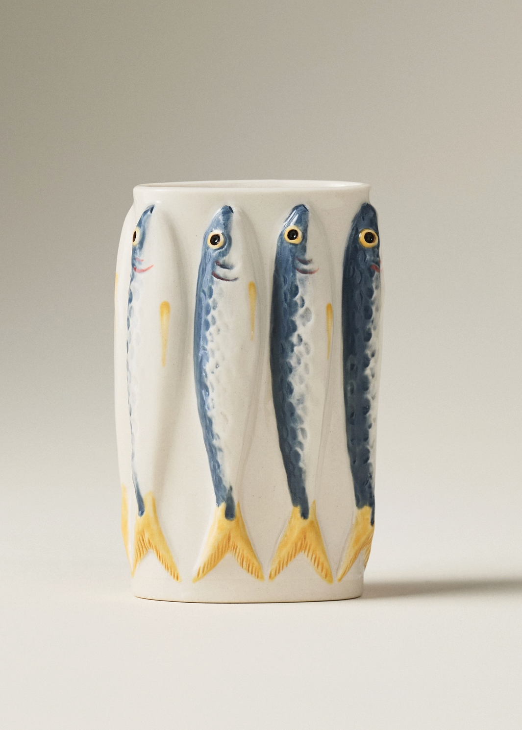 A white ceramic mug decorated with a pattern of four blue and yellow fish, shown against a neutral gray studio background.