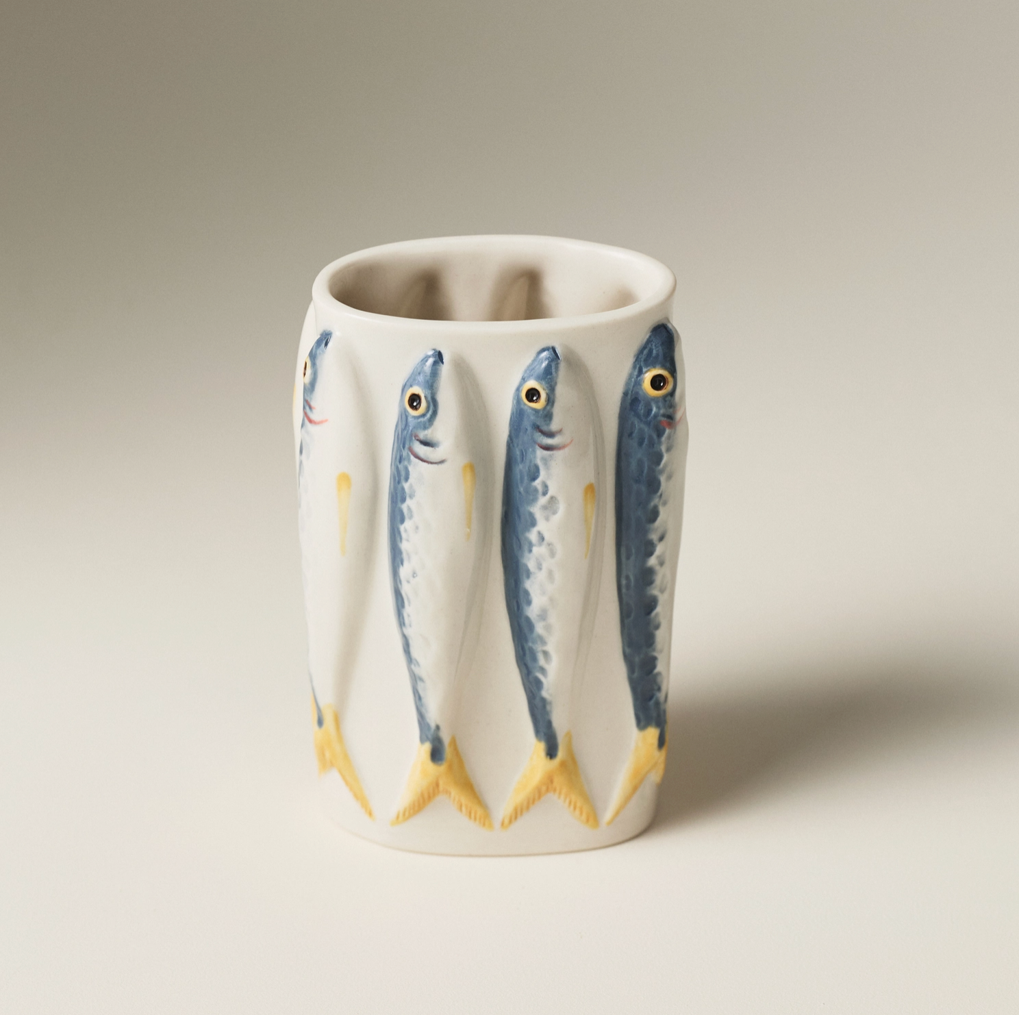 A white ceramic vase decorated with a vertical pattern of three blue and yellow mackerel fish, shown on a neutral light gray background.
