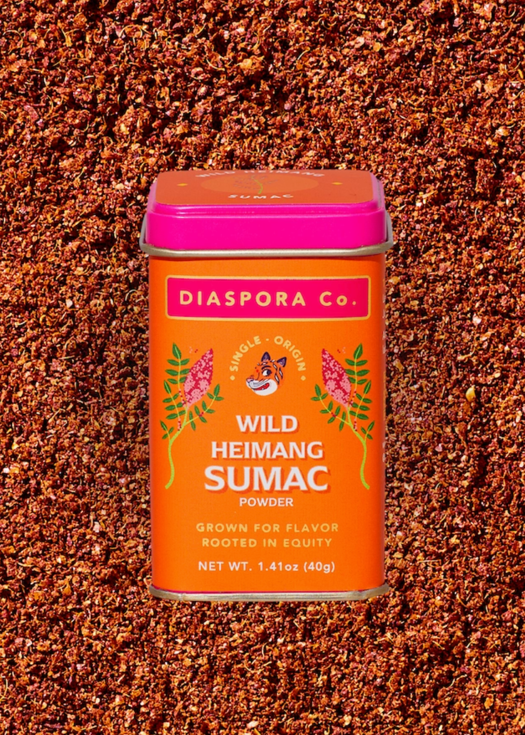 A tin of Diaspora Co. Wild Heimang Sumac Powder centered on a textured background of loose brown sumac berries.
