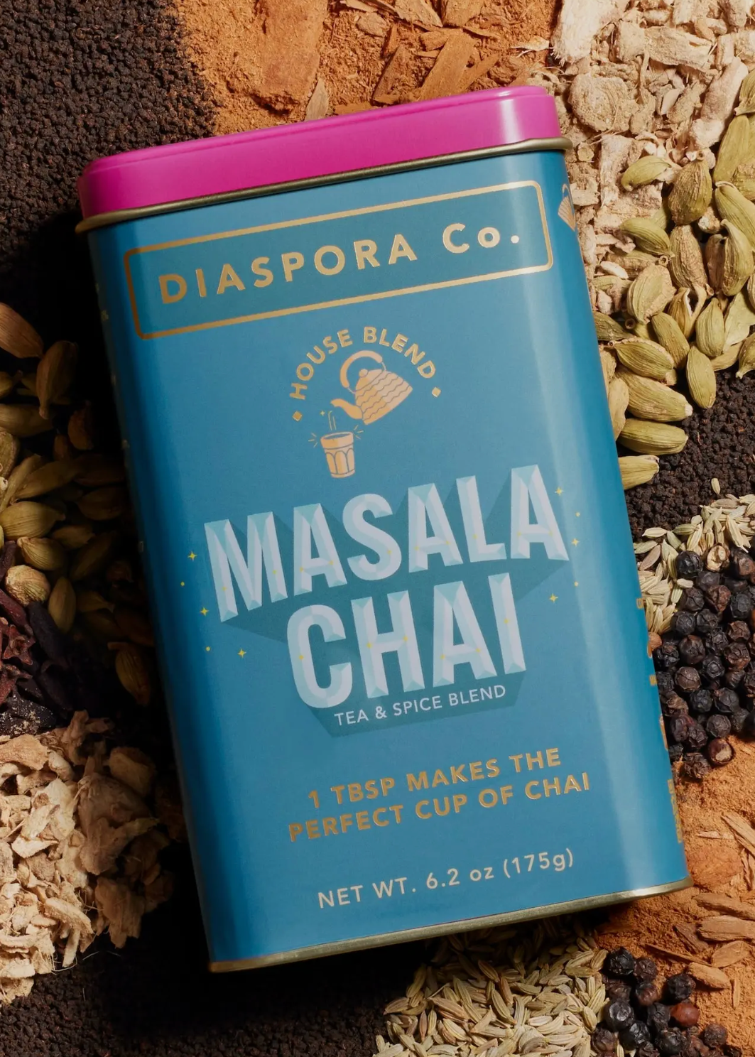 A tin of Diaspora Co. Masala Chai tea blend, featuring a blue label and a magenta lid, styled on a background of whole spices including cardamom, cinnamon, and black peppercorns.