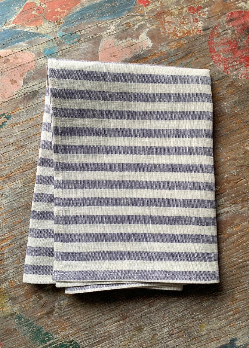 A folded striped fabric cloth with alternating  horizontal stripes, placed on a rustic painted wooden surface.