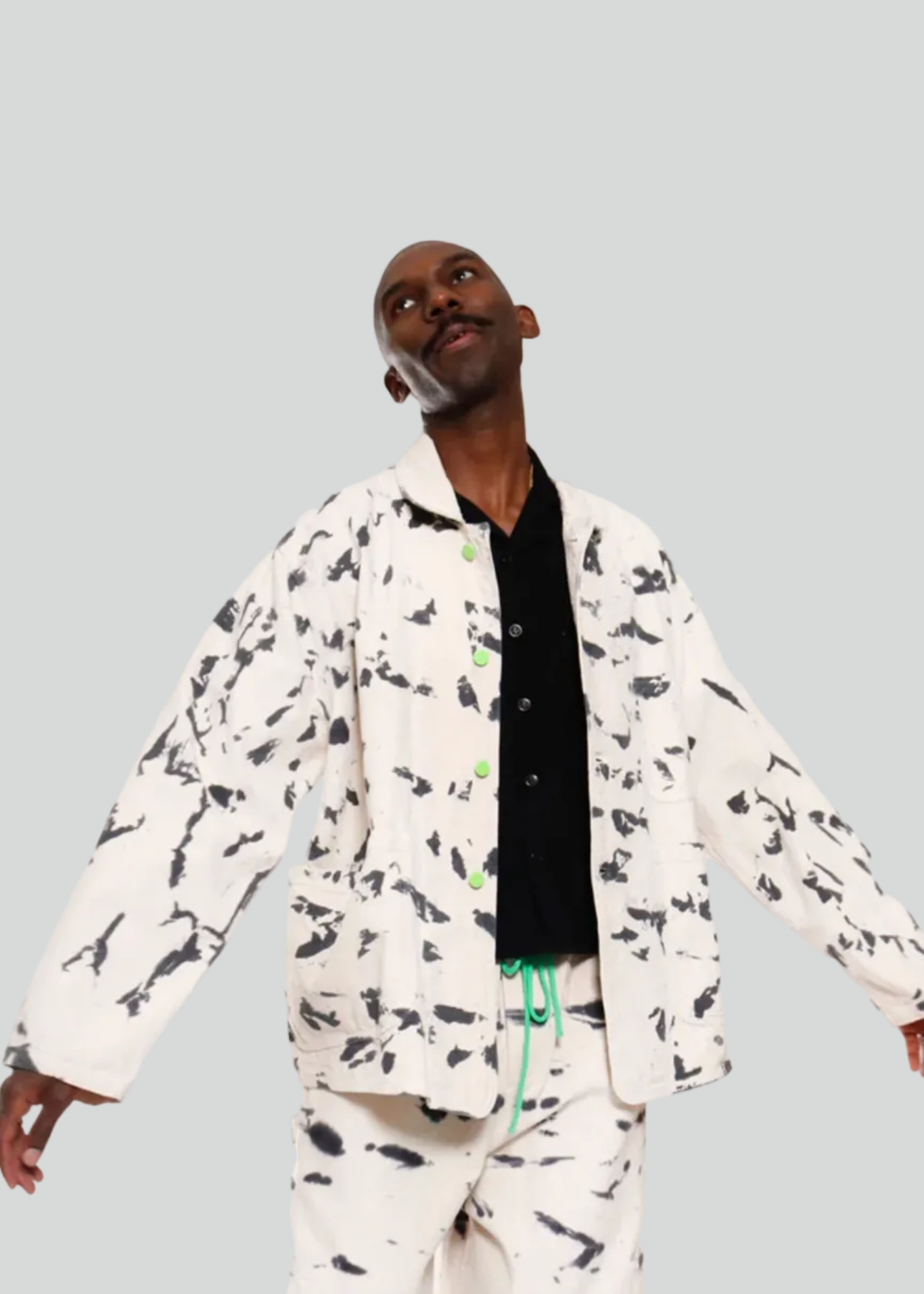 A man modeling a matching two-piece lounge set with a black and white abstract print, featuring a long-sleeve button-up shirt and pants, styled over a black t-shirt.