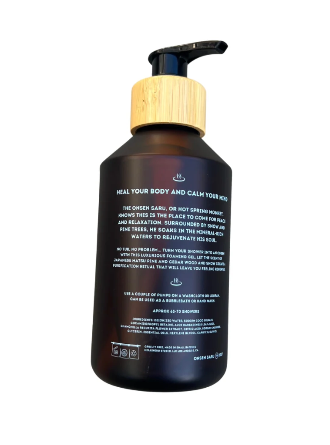 A dark amber glass pump bottle of body wash with a light wood-grain cap and black pump, shown from the back with product text visible, on a white background.