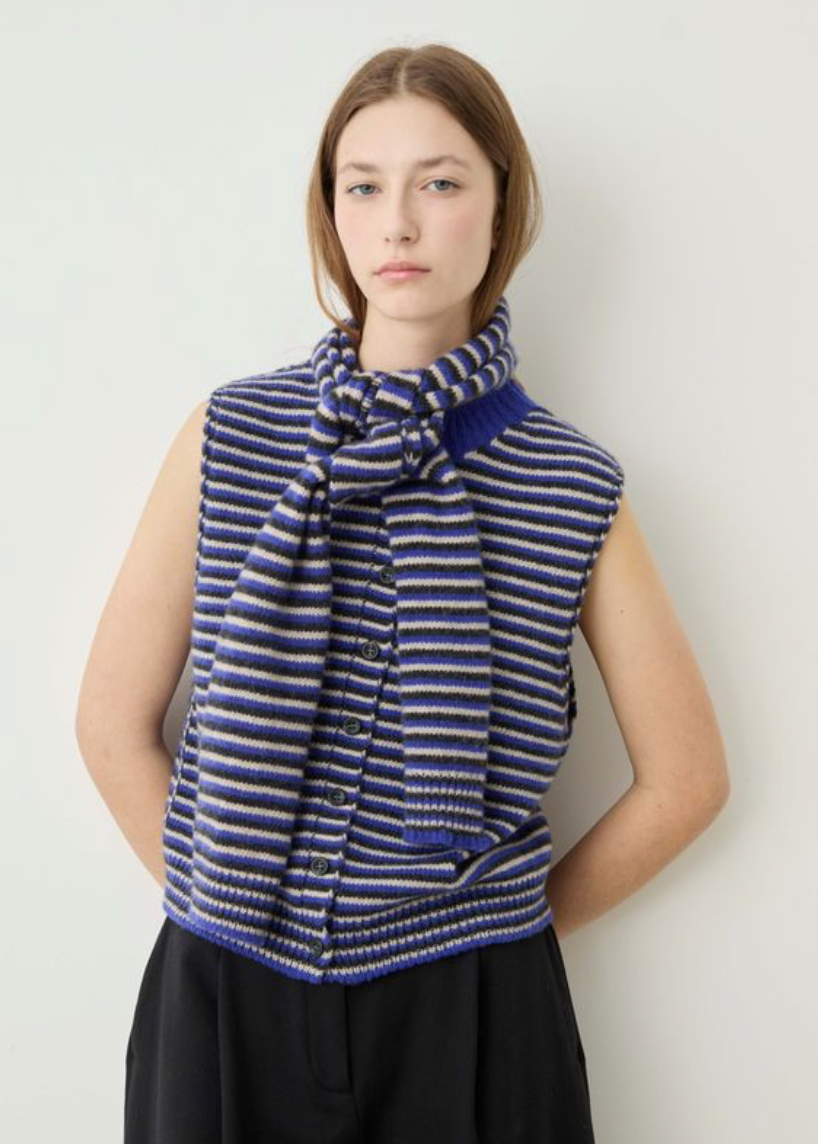 A model wearing a sleeveless knit vest and matching knotted scarf in a blue, purple, and white stripe pattern, set against a plain light gray background.