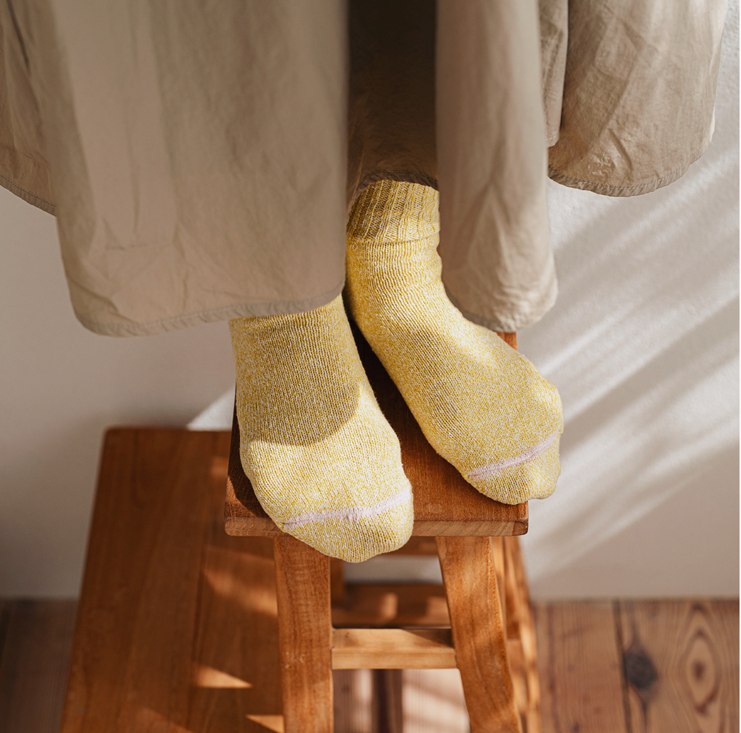 A person wearing textured yellow socks with a subtle lavender stripe, standing on a wooden stool in warm natural light.