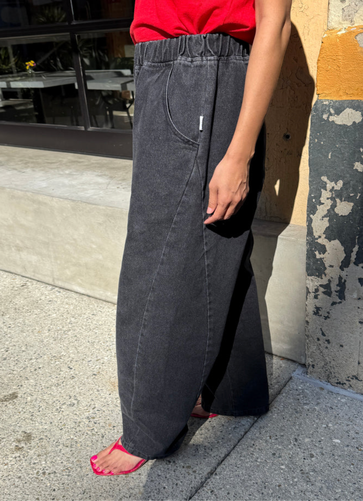 A person wearing wide-leg charcoal gray denim pants with an elastic waistband, standing outdoors on a concrete sidewalk next to a building wall.
