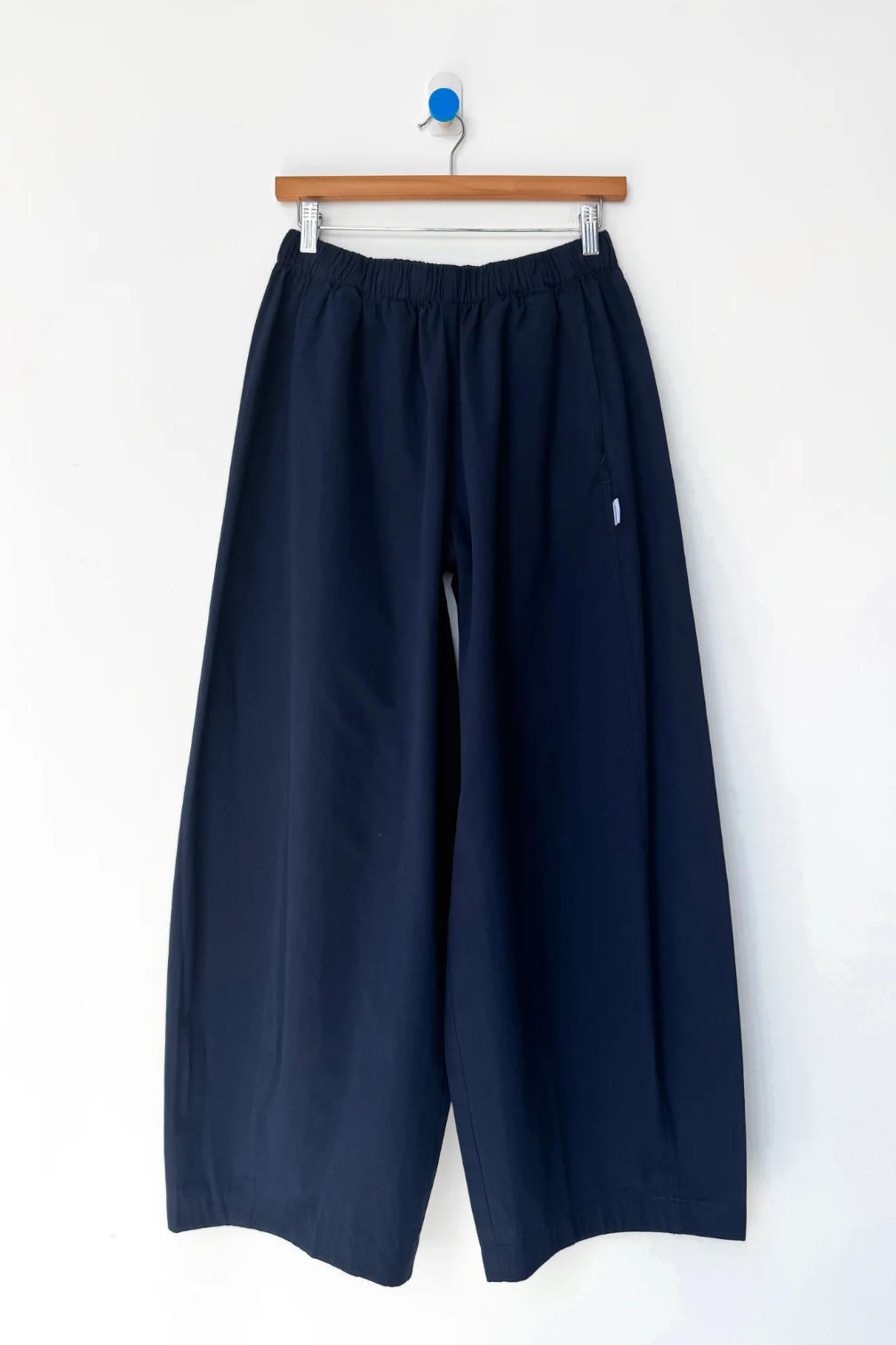 Navy blue wide-leg cropped pants hanging from a wooden hanger against a plain white wall.