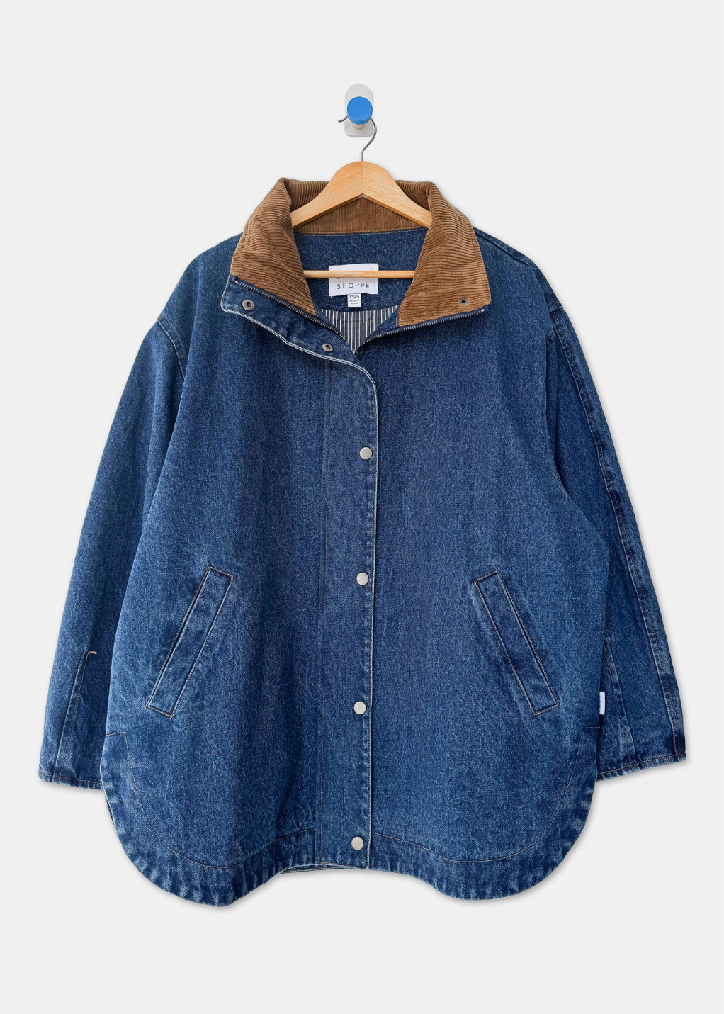 A blue denim jacket with a brown corduroy collar, hanging on a wooden hanger against a light gray background.
