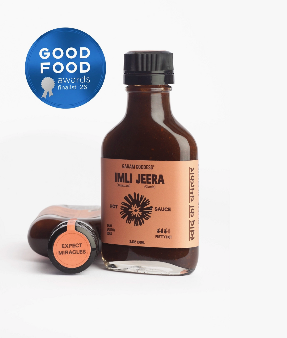 A bottle of Hot Sauce with its cap placed beside it on a white background, featuring a blue 'Good Food Awards finalist 26' badge overlay.