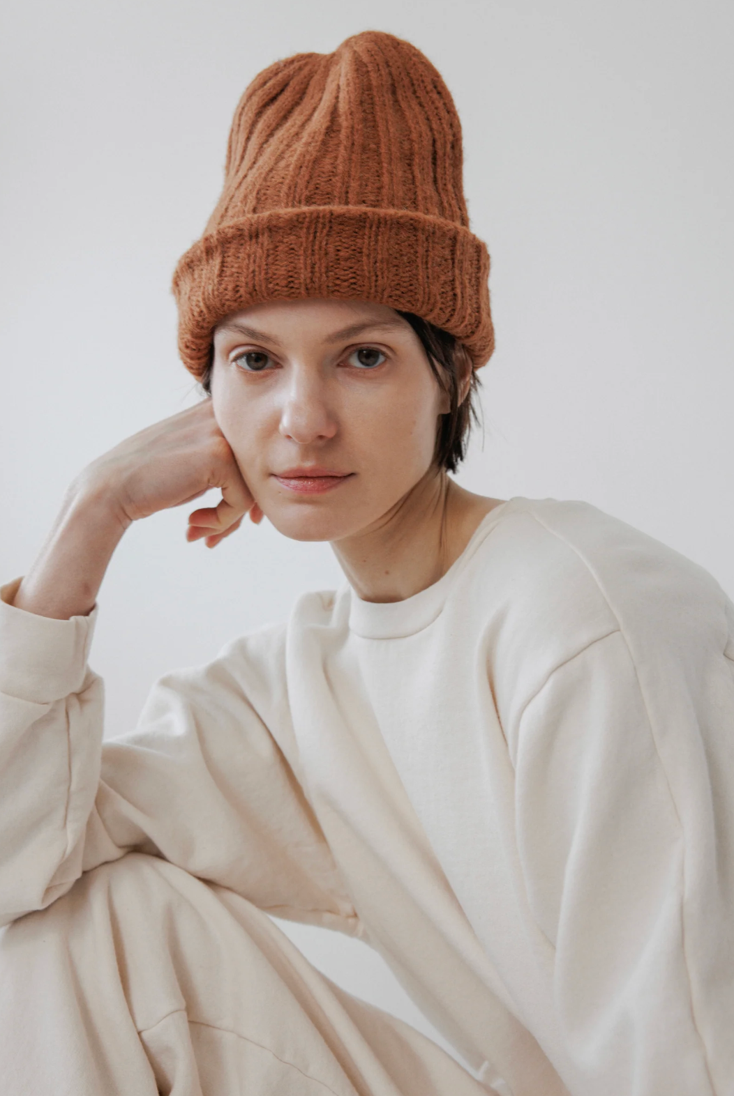 person in white wearing a pointy alpaca hat in a rust color 