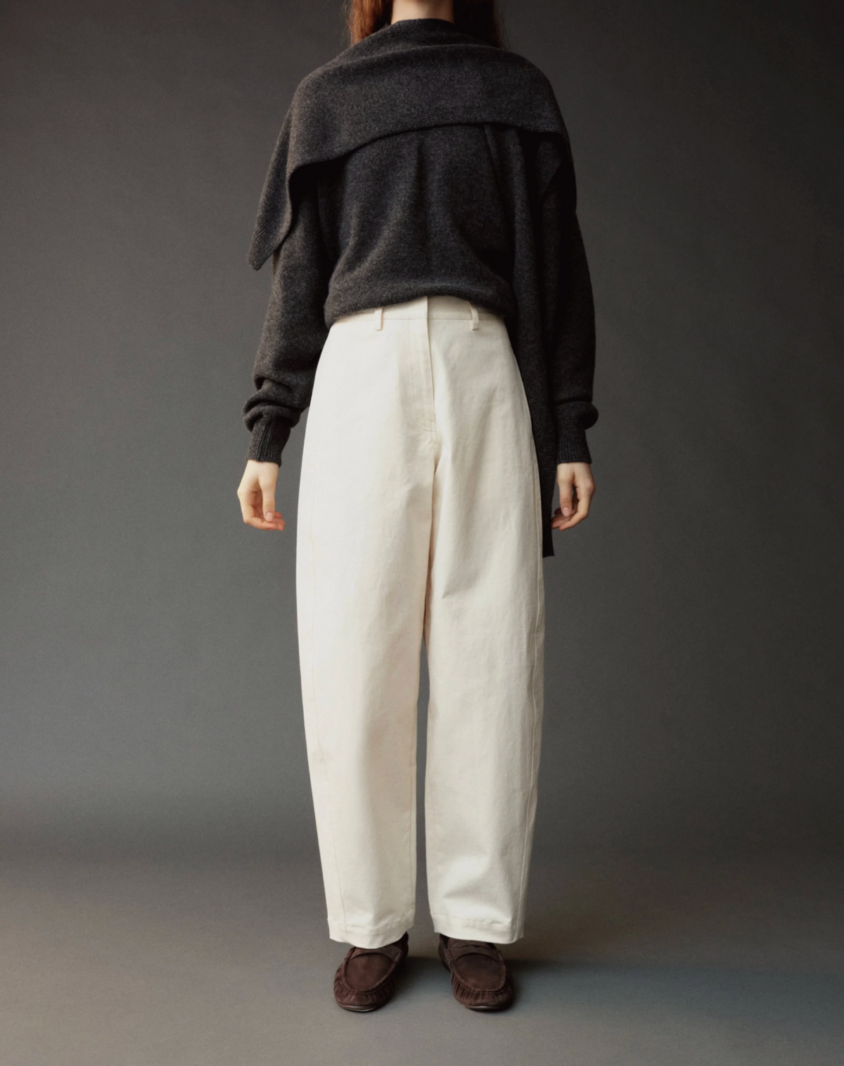 Person wearing a dark sweater and white pants against a gray background