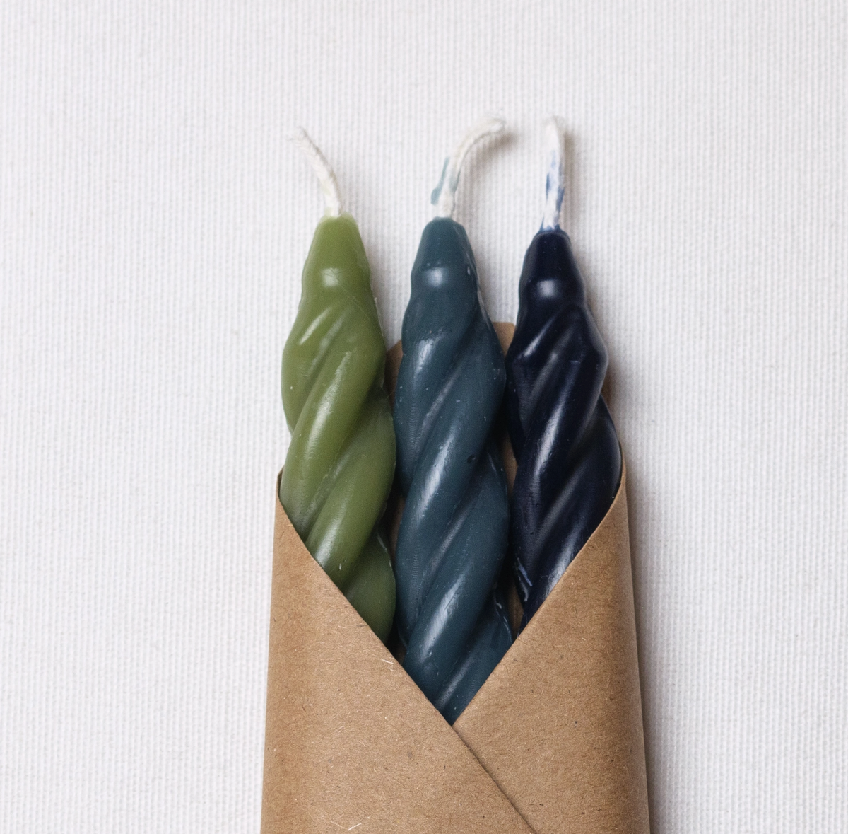 3 complementary shades of green beeswax candles in a craft wrapper with a white informational label