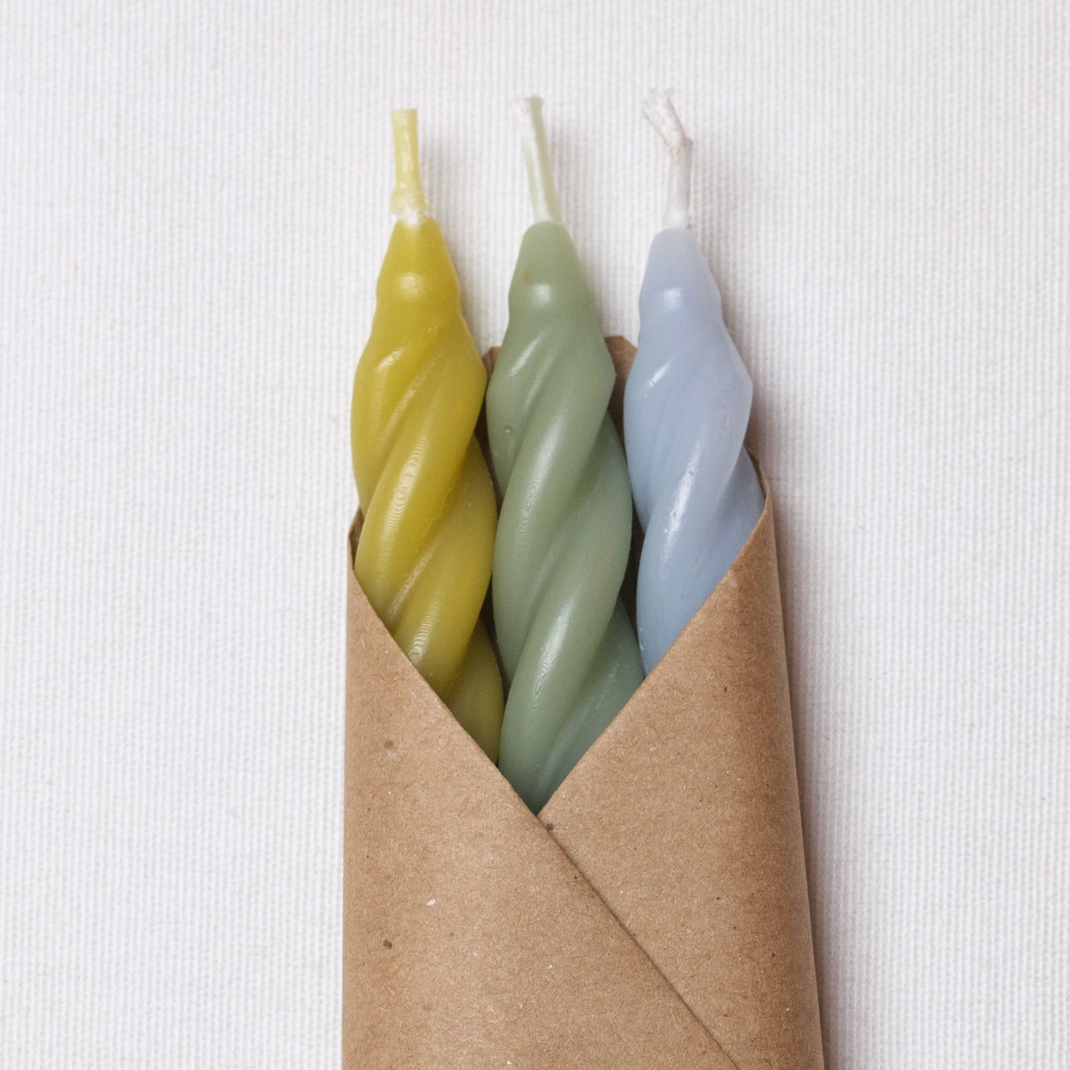 a yellow green, green and sky blue trio of candles in brown paper 