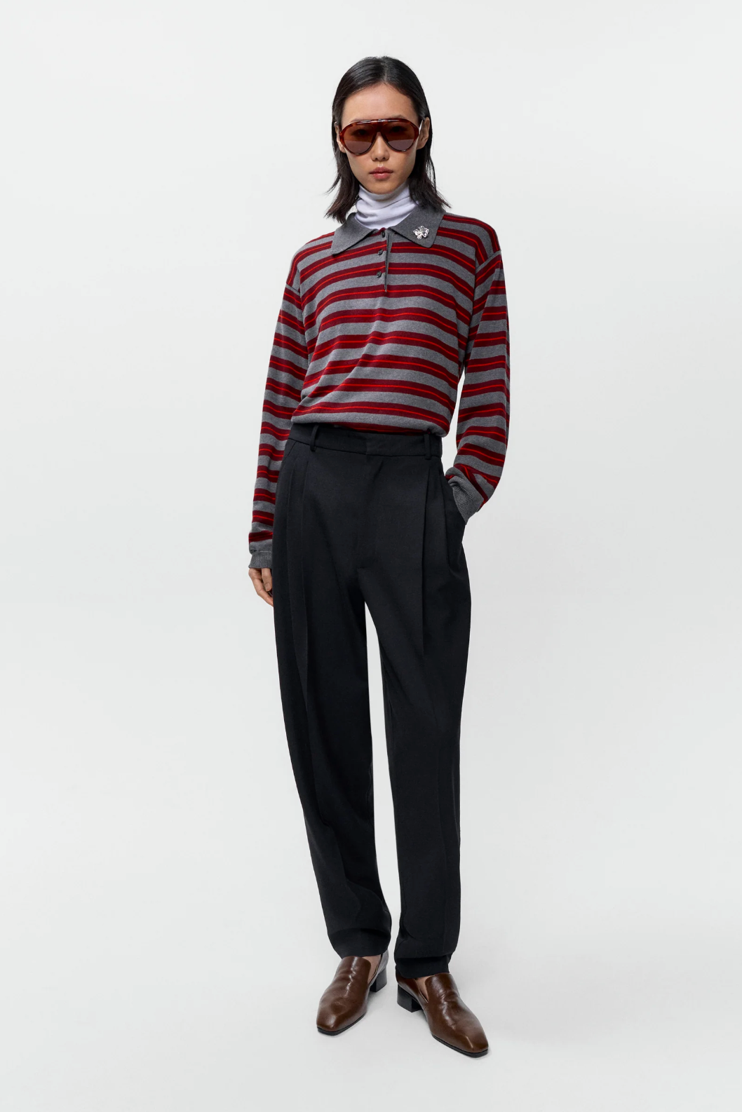 grey and red striped polo on model wearing black pants, brown shoes and sunglasses