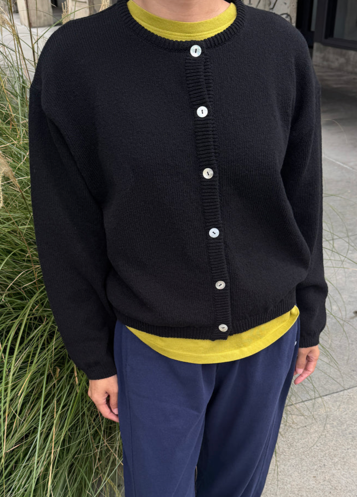 model wearing black cardigan with neon yellow underneath and navy sweatpants