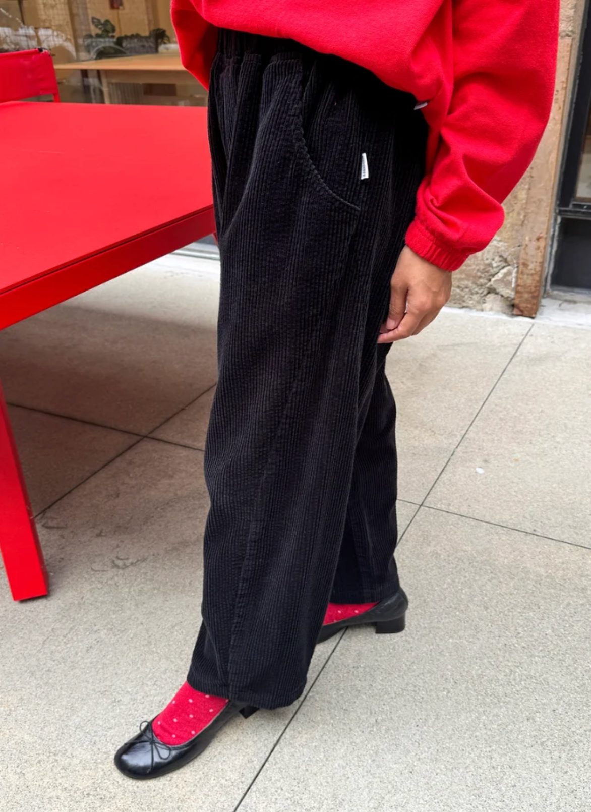 model wearing black cords with red socks and black ballet flats and red sweater.