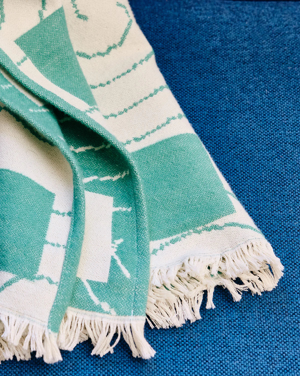 Teal and white patterned towel with fringes on a blue background