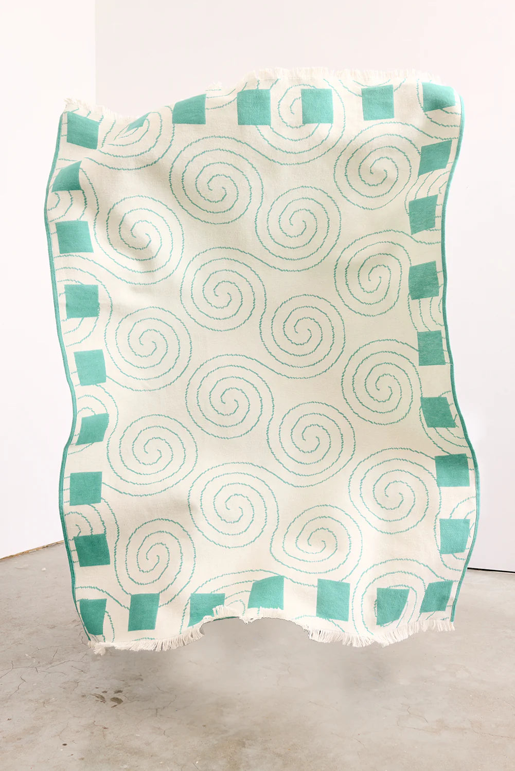 Teal and white patterned blanket on a light wooden floor.
