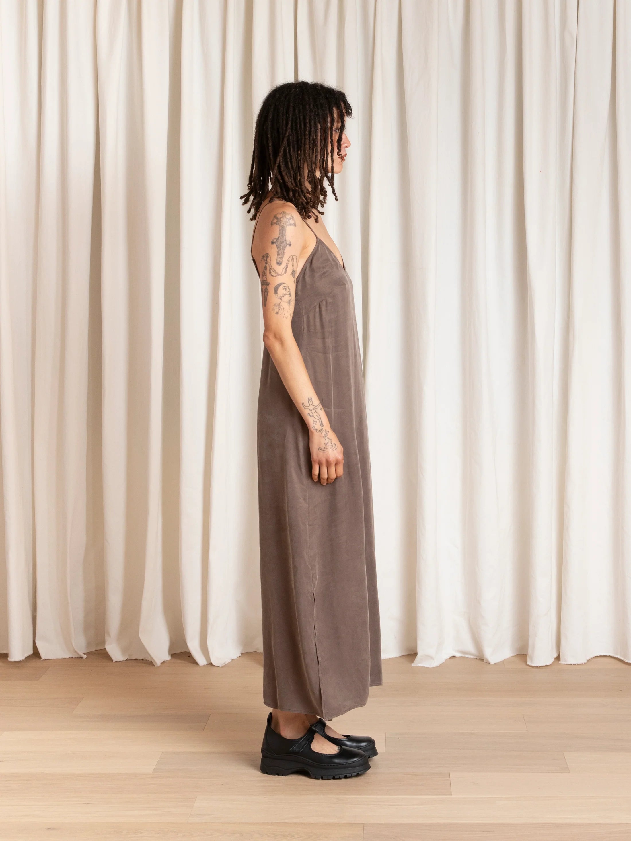 Person wearing a brown dress standing in front of white curtains