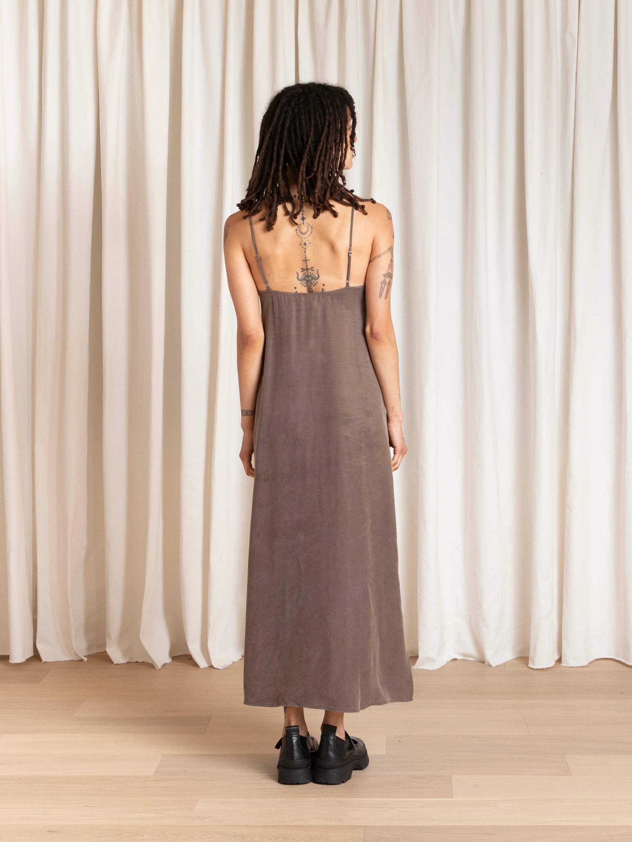 Person wearing a brown slip dress standing in front of white curtains.