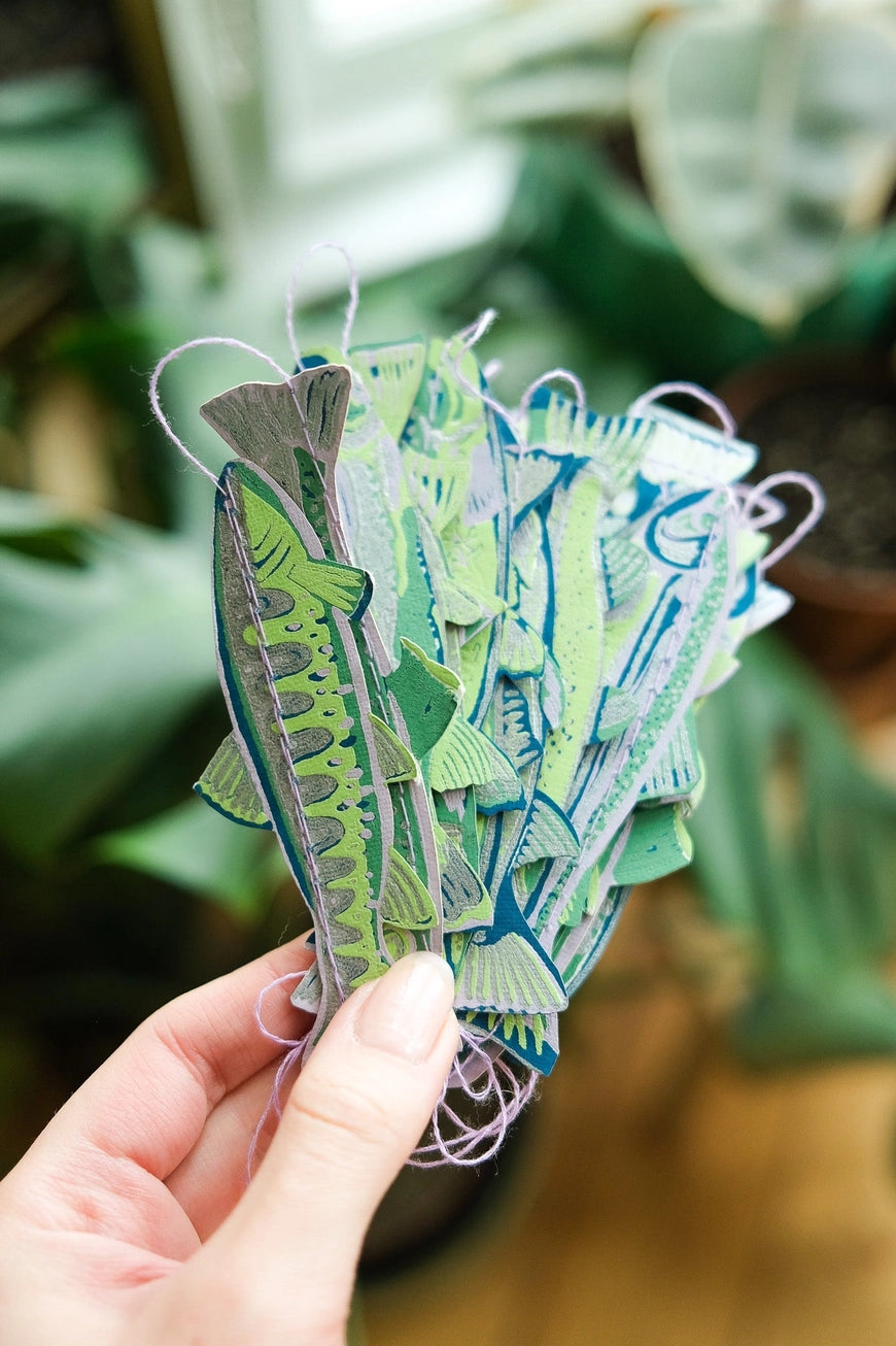 Hand holding a stack of colorful paper fish with a blurred green plant background