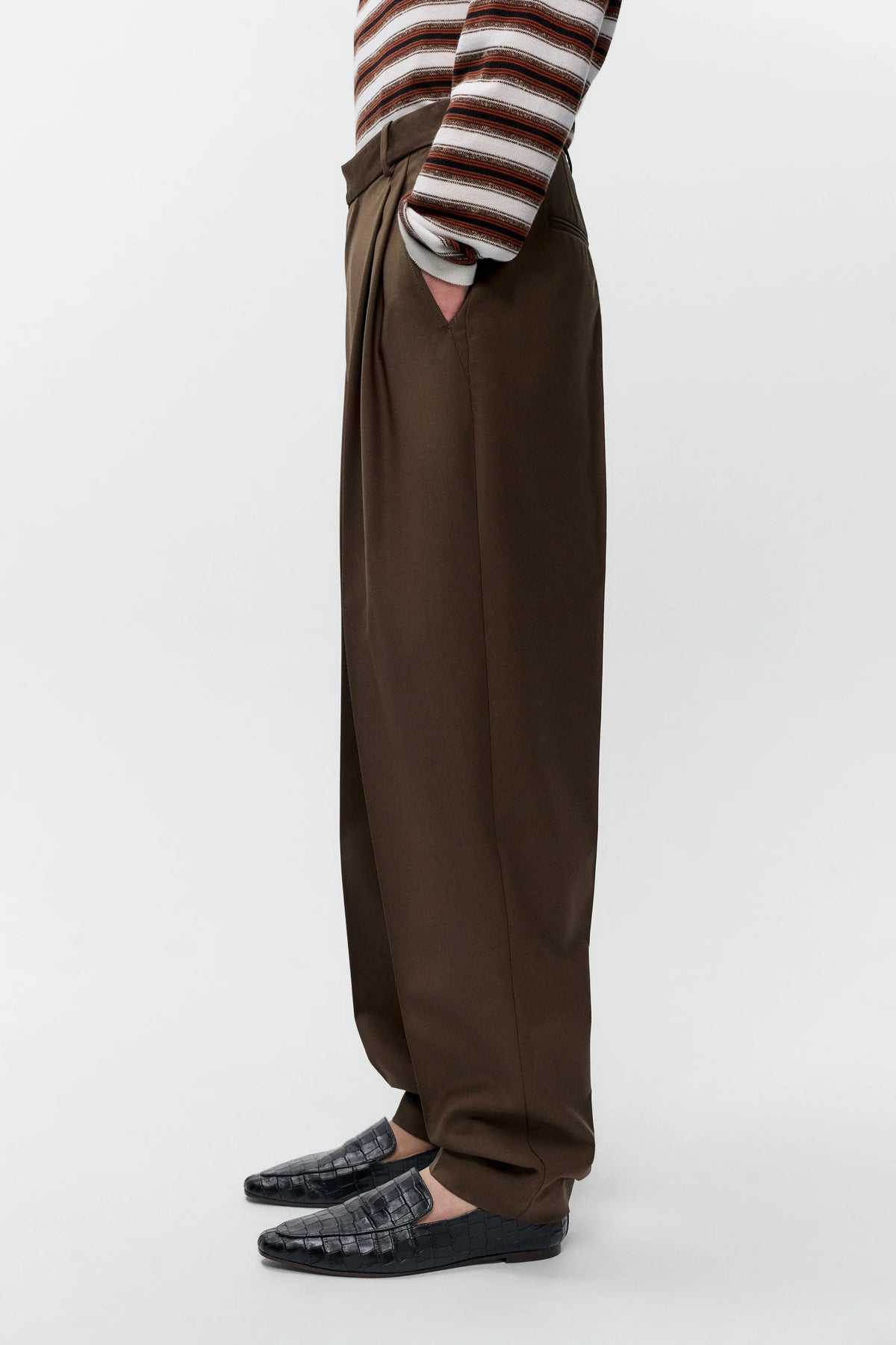 Person wearing brown wide-leg pants and a striped shirt on a white background