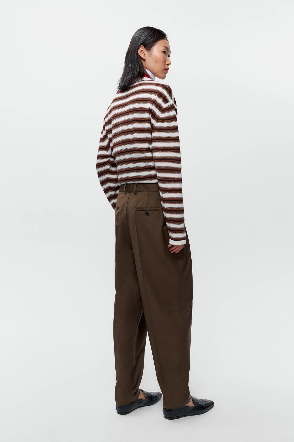 Person wearing a striped sweater and brown pants on a white background