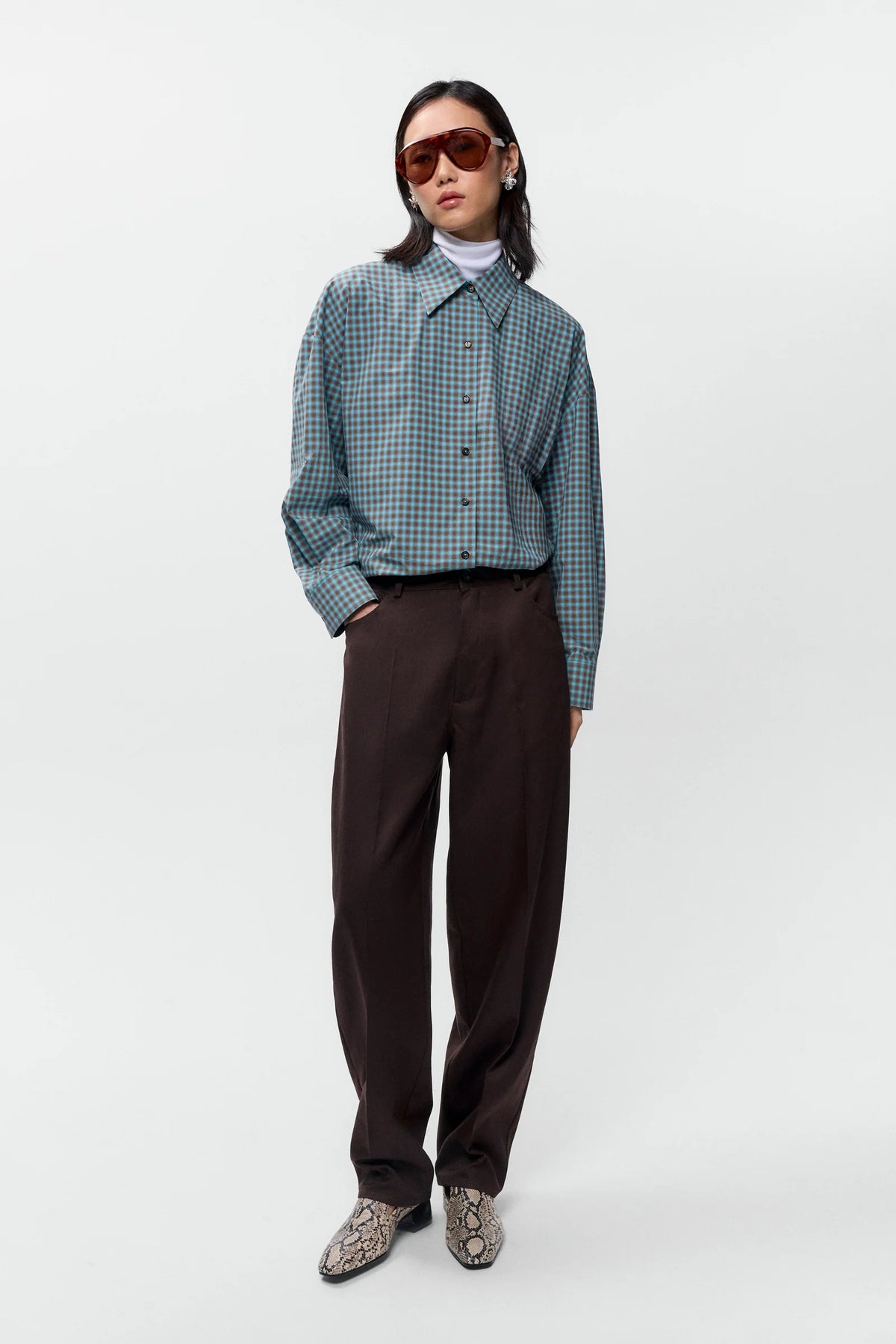 Person wearing a green checkered shirt, brown pants, and sunglasses on a white background