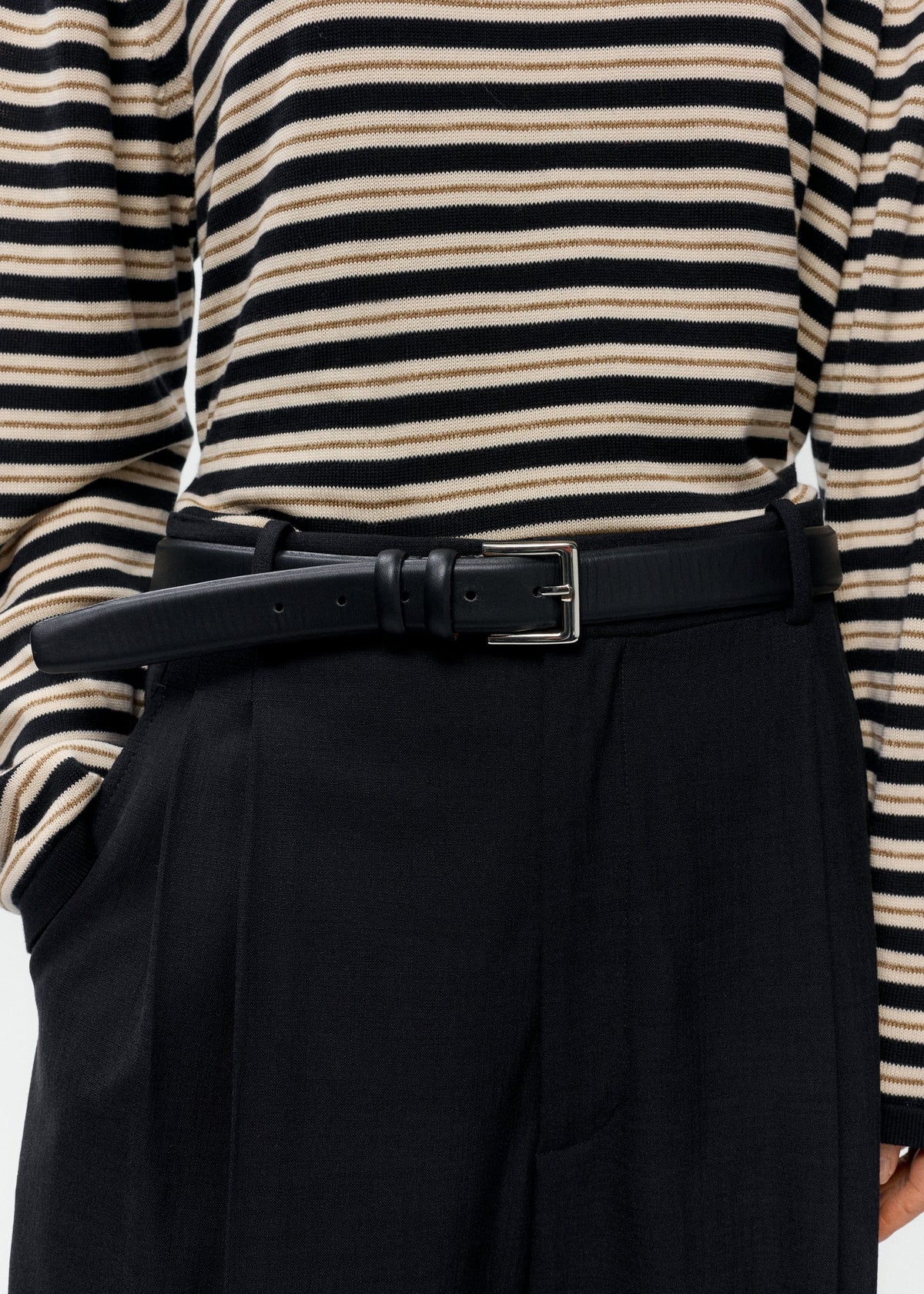 Person wearing a black and white striped shirt with a black belt and black pants on a white background