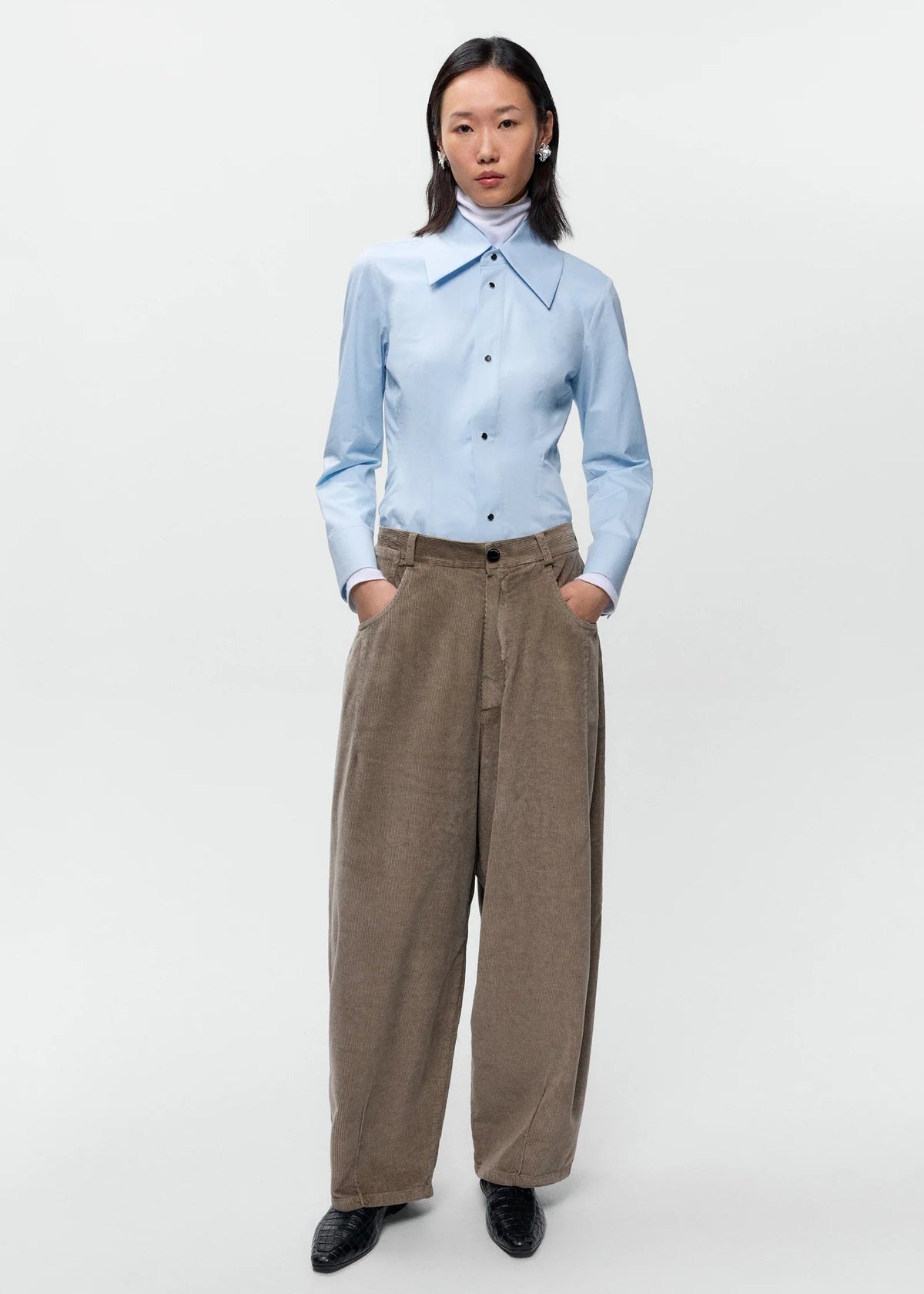 Person wearing a light blue shirt and brown pants on a white background
