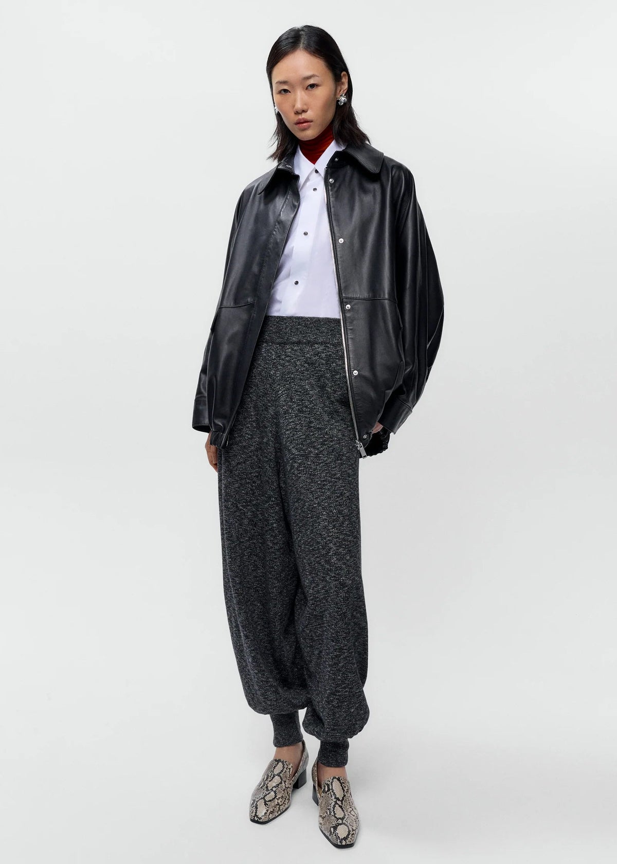 Person wearing a black leather jacket, white shirt, and gray pants on a white background