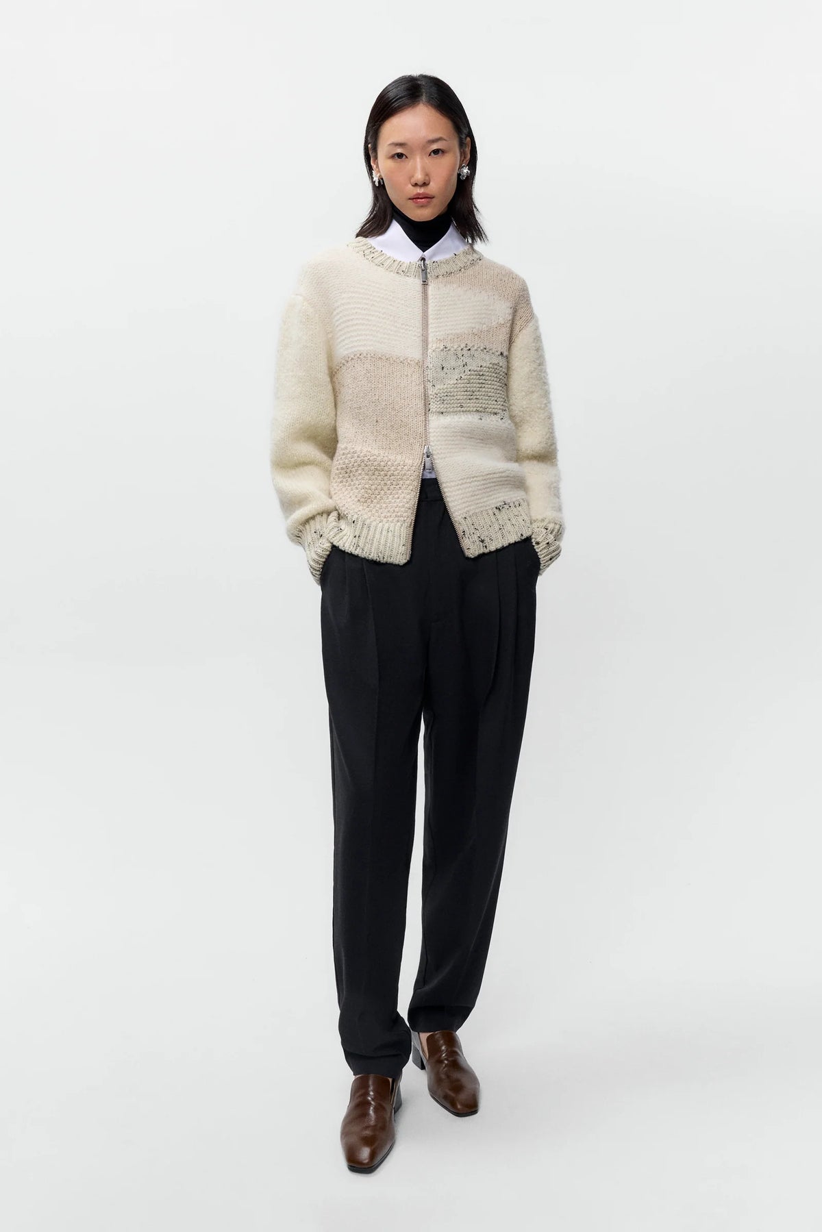Person wearing a cream knitted cardigan over a black outfit on a white background