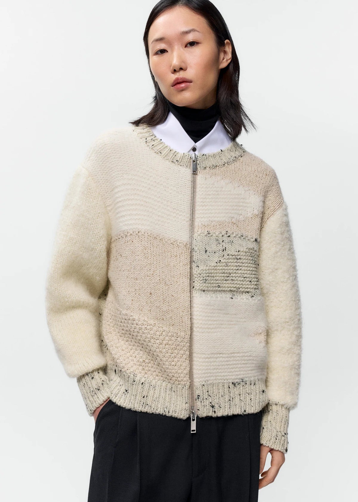 Woman wearing a beige zip-up sweater with a textured pattern on a white background