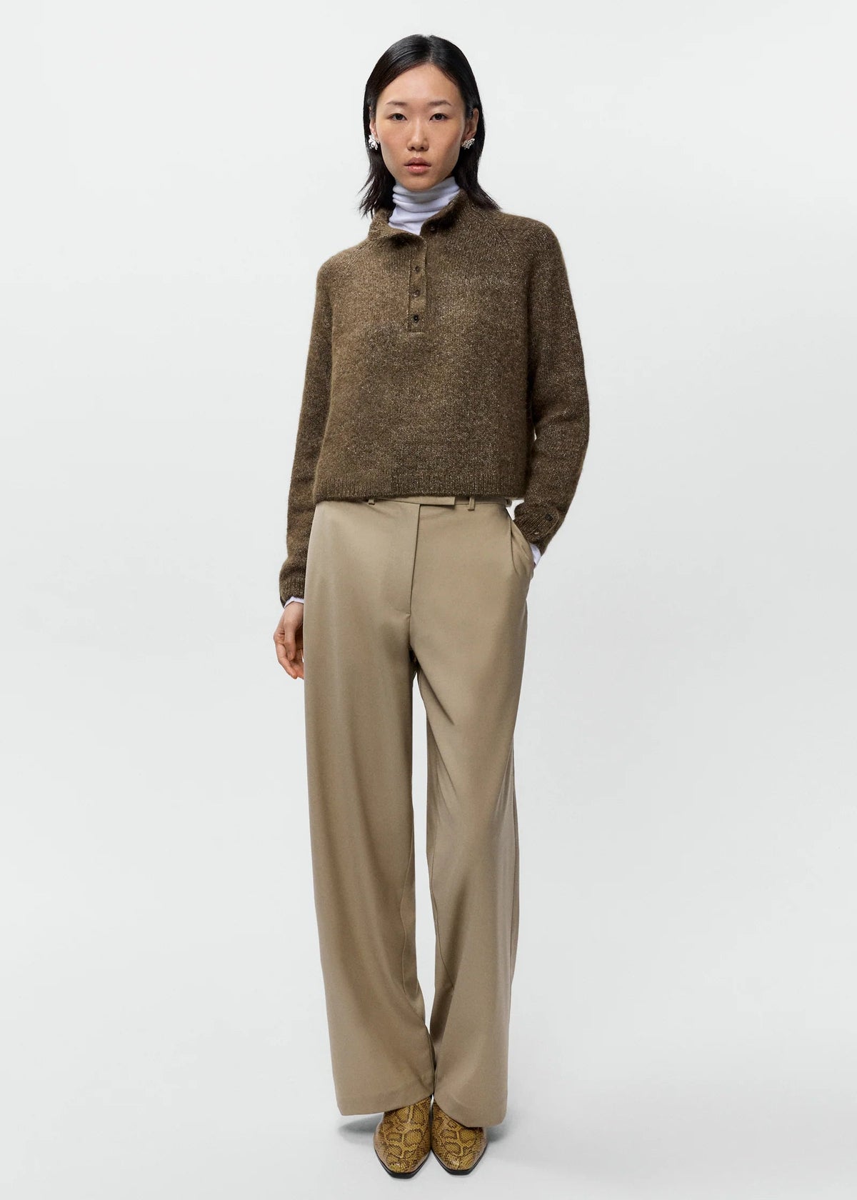 Person wearing a brown sweater and beige pants on a white background