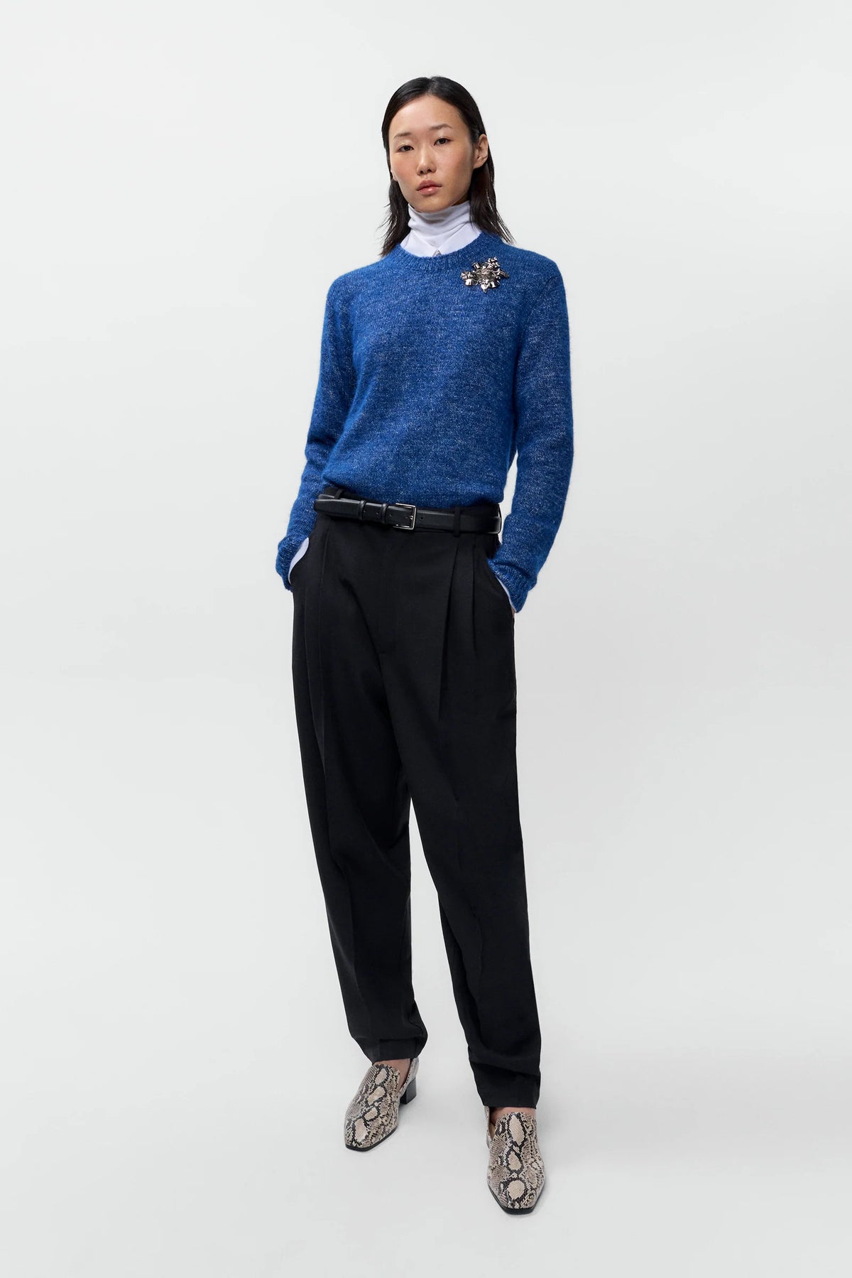 Person wearing a blue sweater, black pants, and patterned shoes on a white background