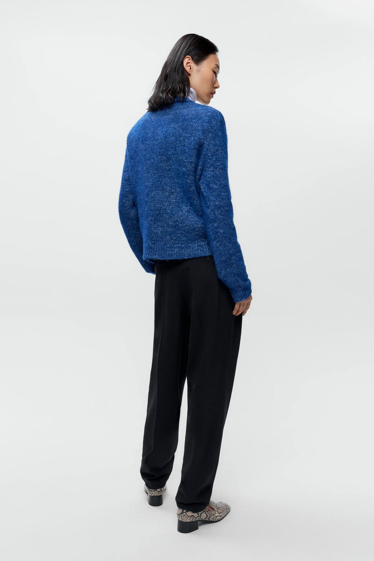 Person wearing a blue knitted sweater and black pants on a white background