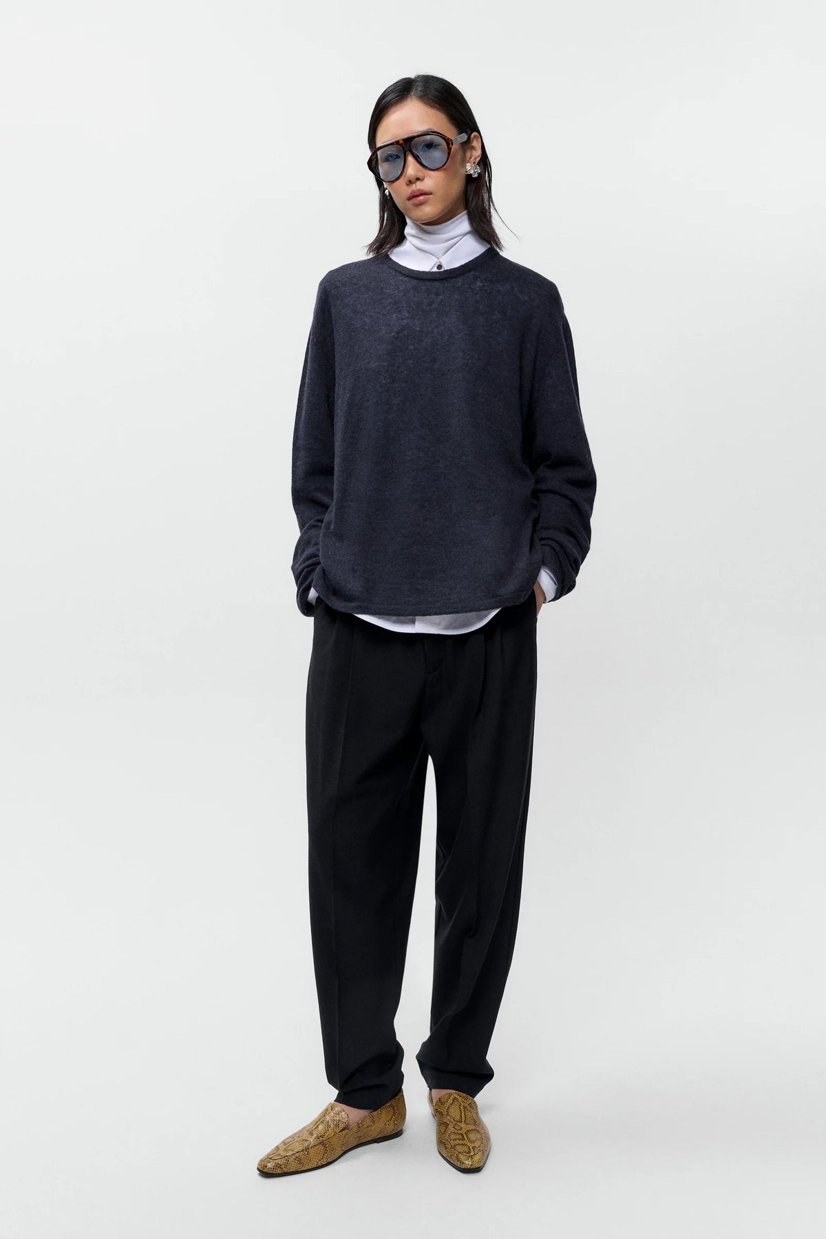 Person wearing a dark sweater, black pants, and brown shoes on a white background