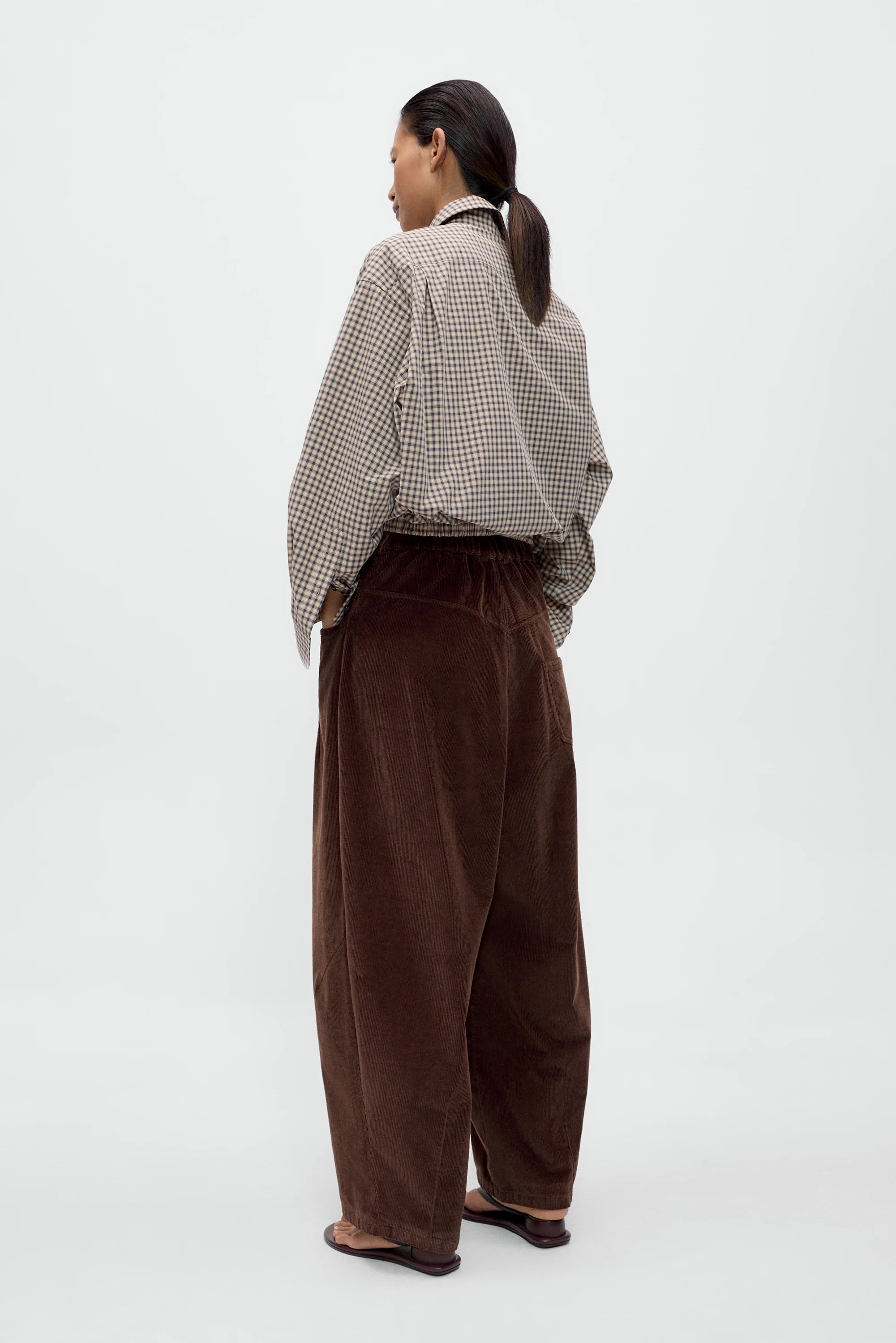 Person wearing a checkered shirt and brown pants on a white background