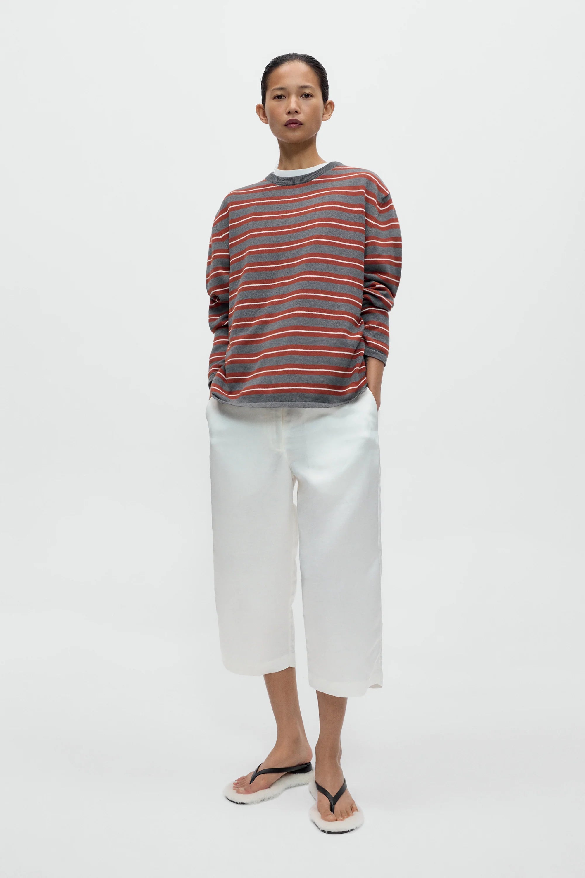 Person wearing a striped sweater and white pants on a plain background