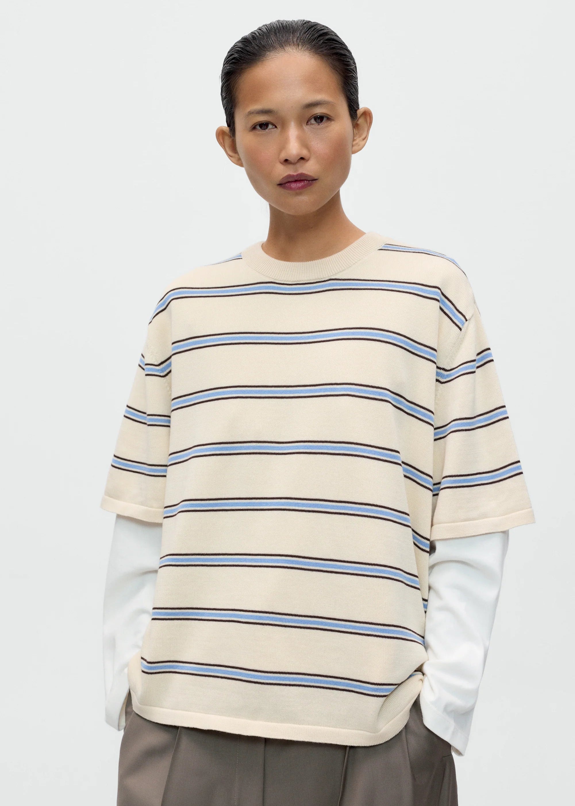 Person wearing a cream and blue striped sweater with a plain background
