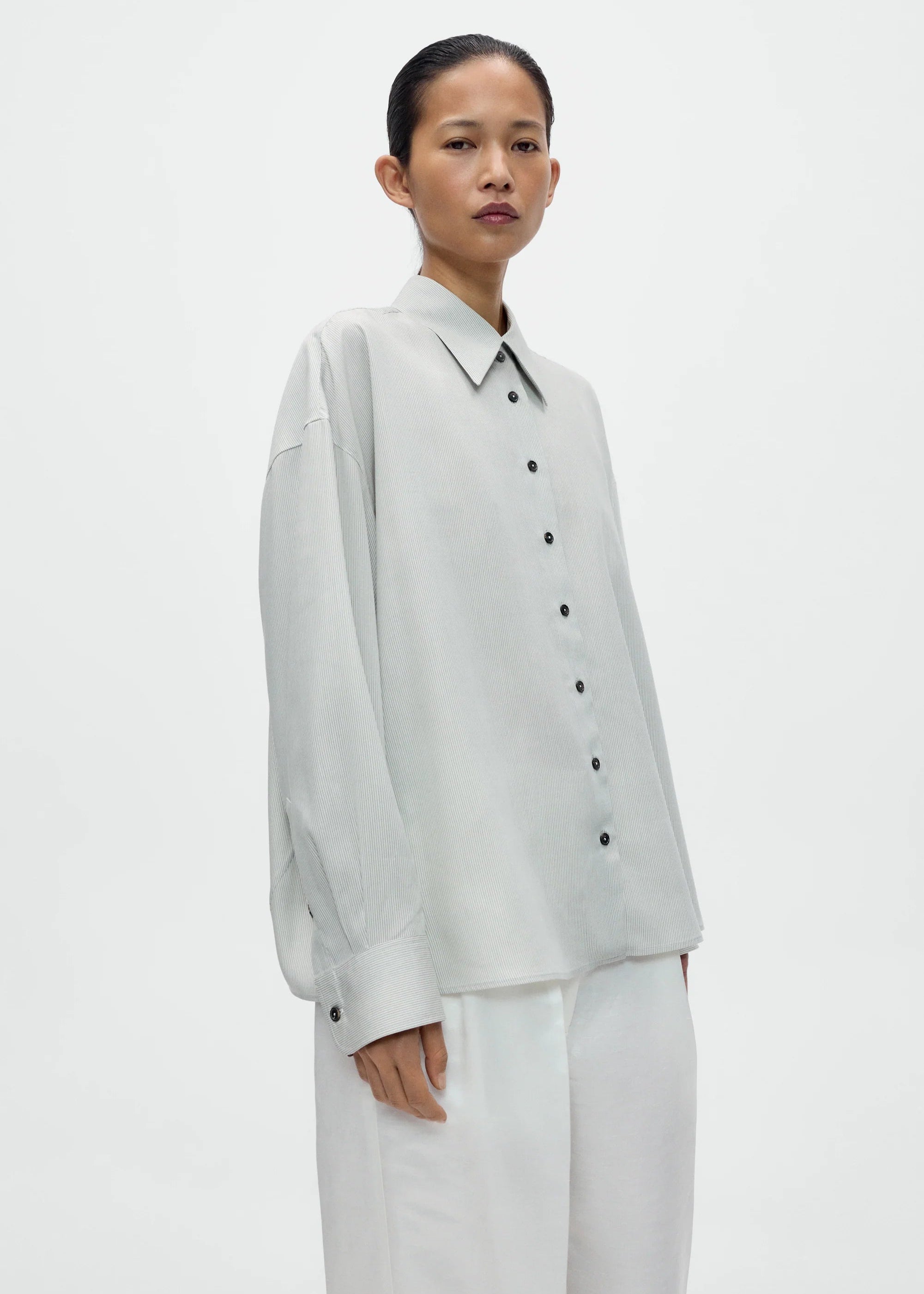 Person wearing a light gray button-up shirt and white pants on a plain background