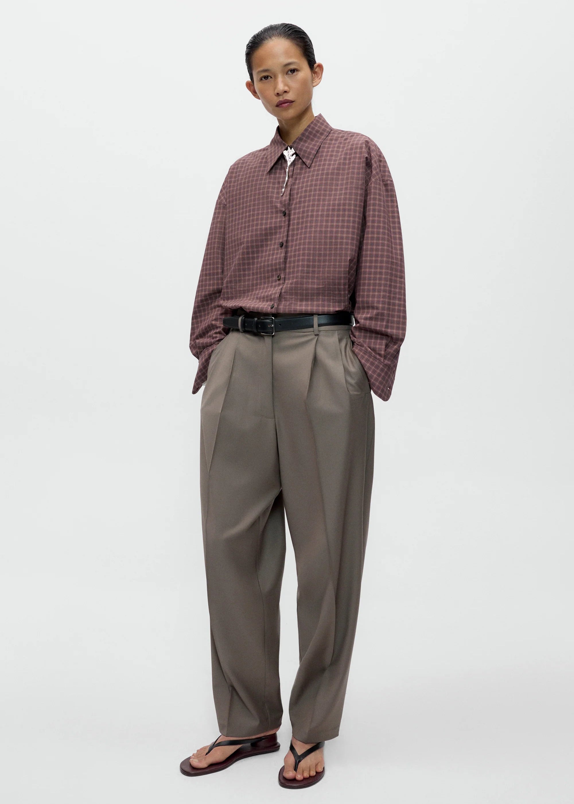 Person wearing a plaid shirt and beige pants on a white background