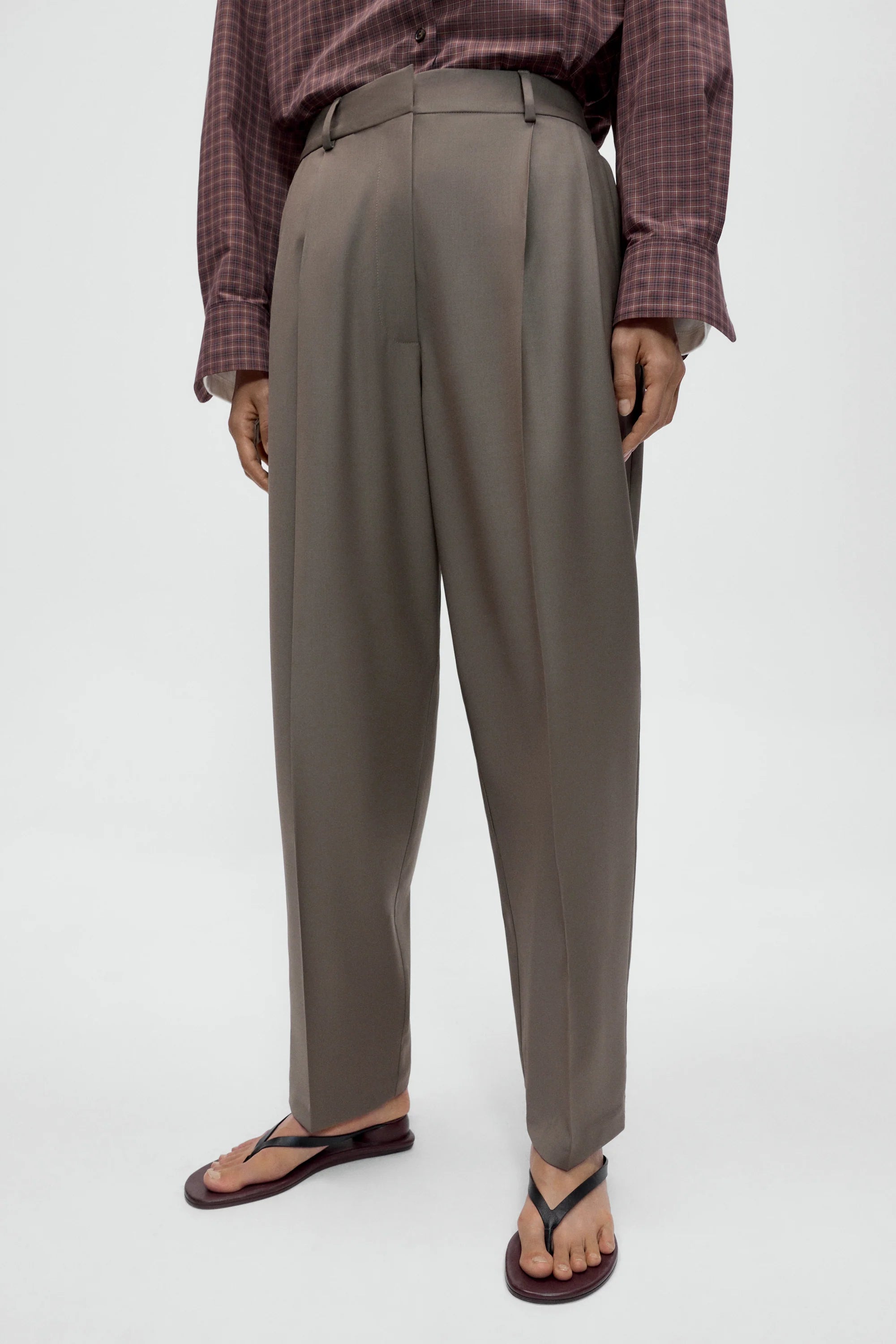 Person wearing gray high-waisted pants and a plaid shirt on a white background