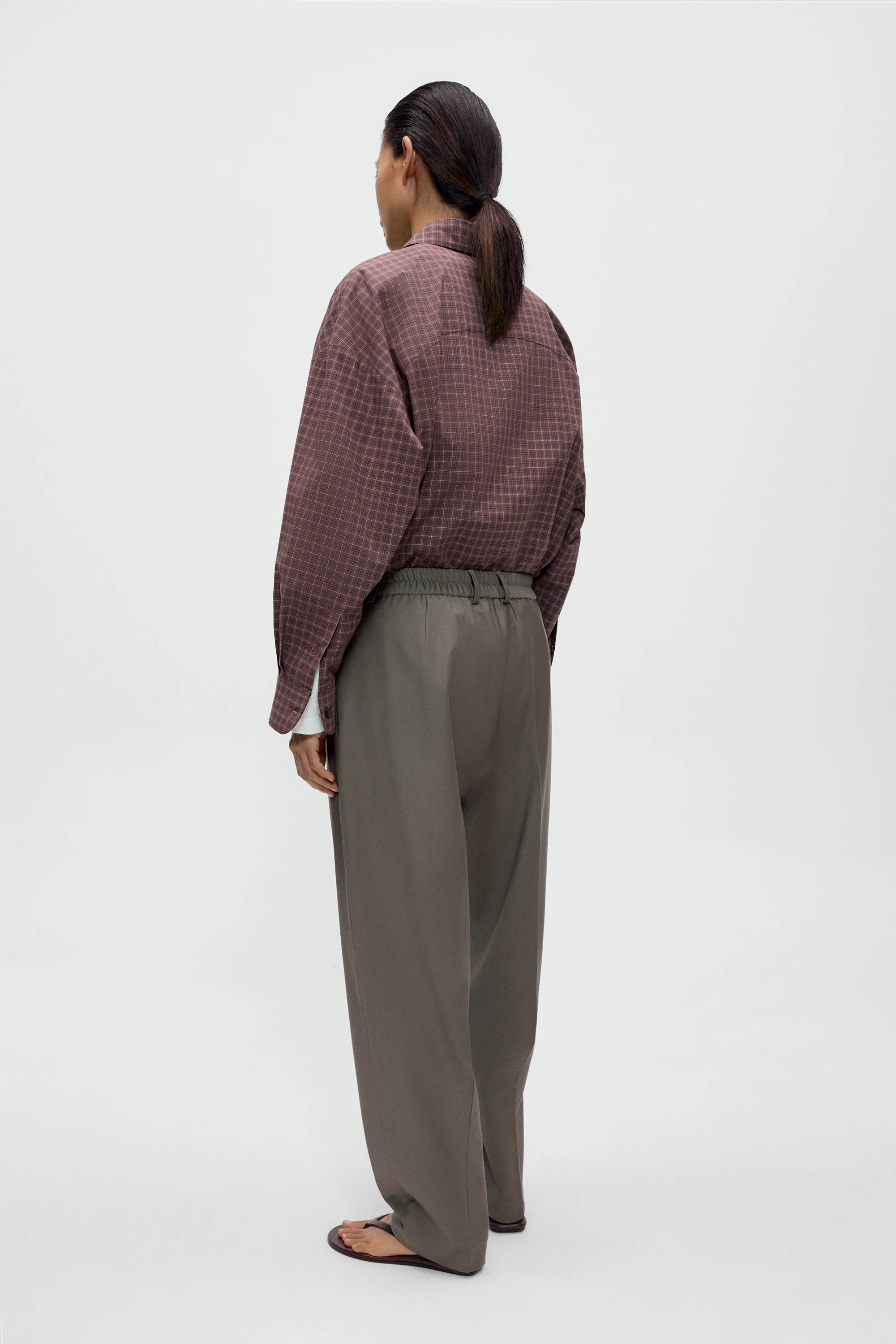 Person wearing a patterned shirt and gray pants on a white background