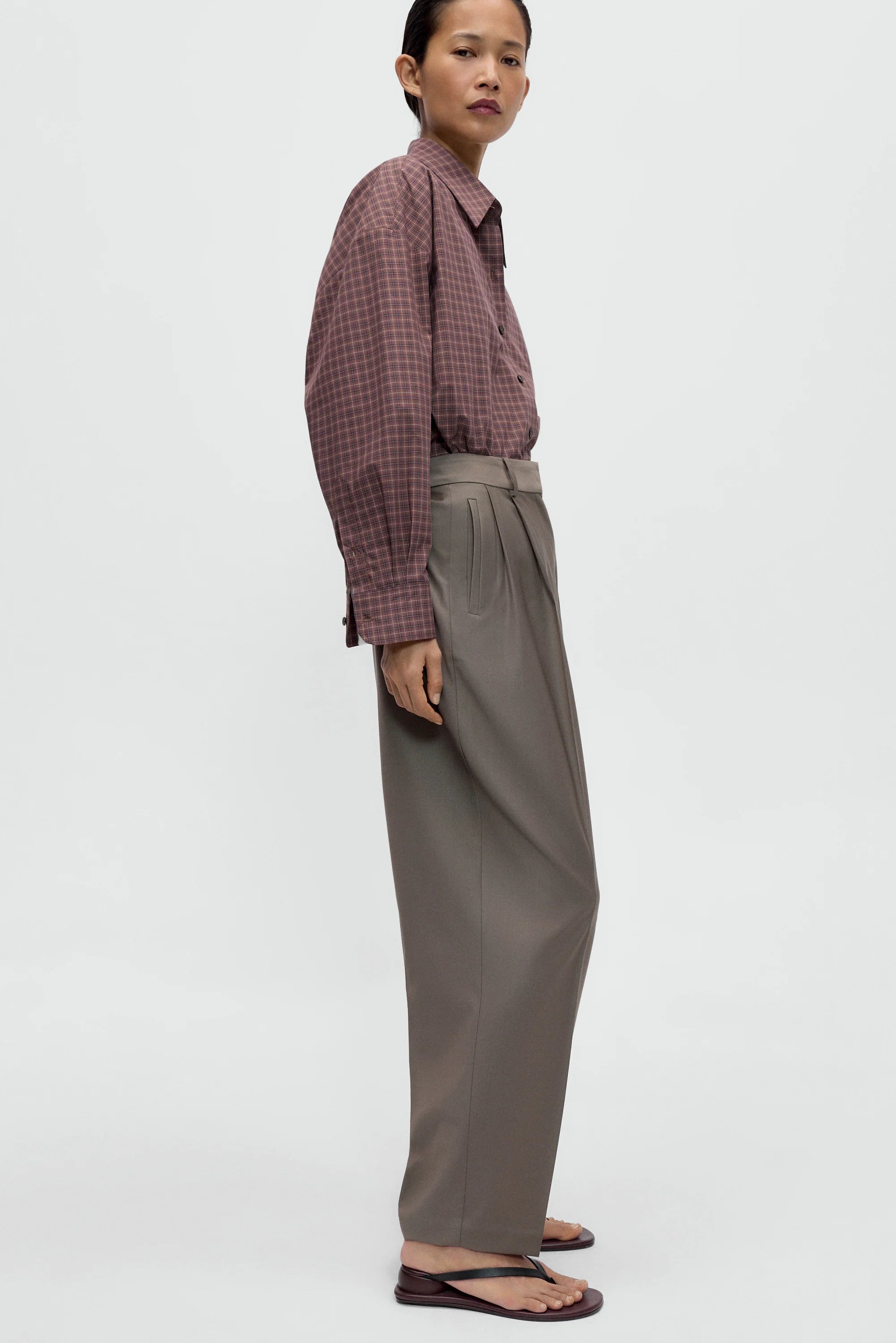 Person wearing a checkered shirt and gray pants on a white background