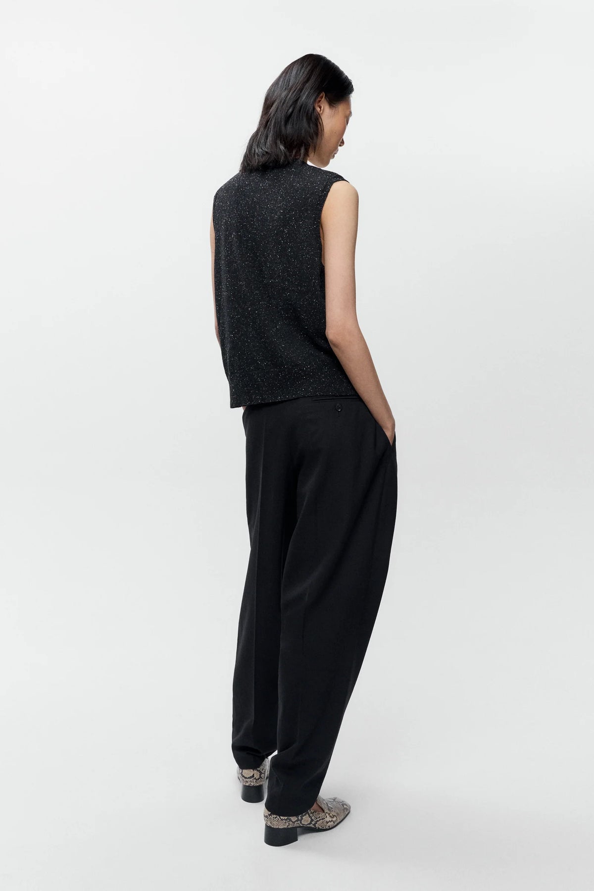 Person wearing a black sleeveless top and black pants on a white background