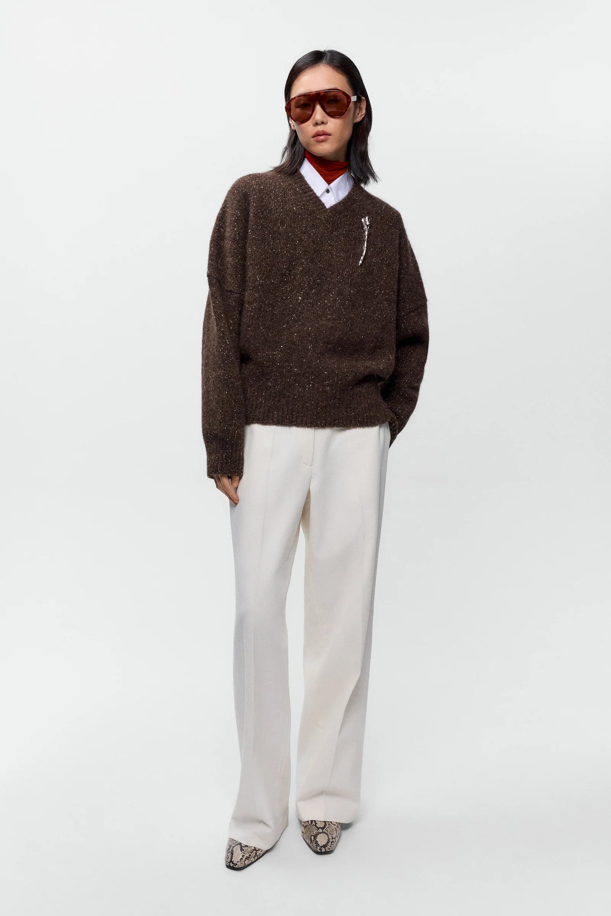 Person wearing a brown sweater and white pants on a white background