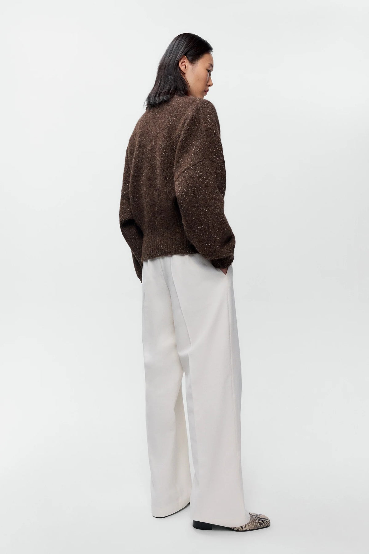 Person wearing a brown sweater and white pants on a white background